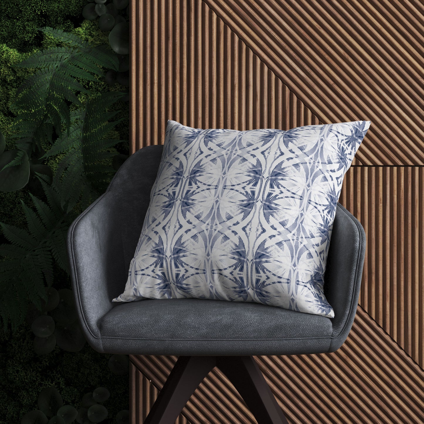 Blue and white abstract pattern pillow sitting on a blue chair in front of a leafy and textured wall.