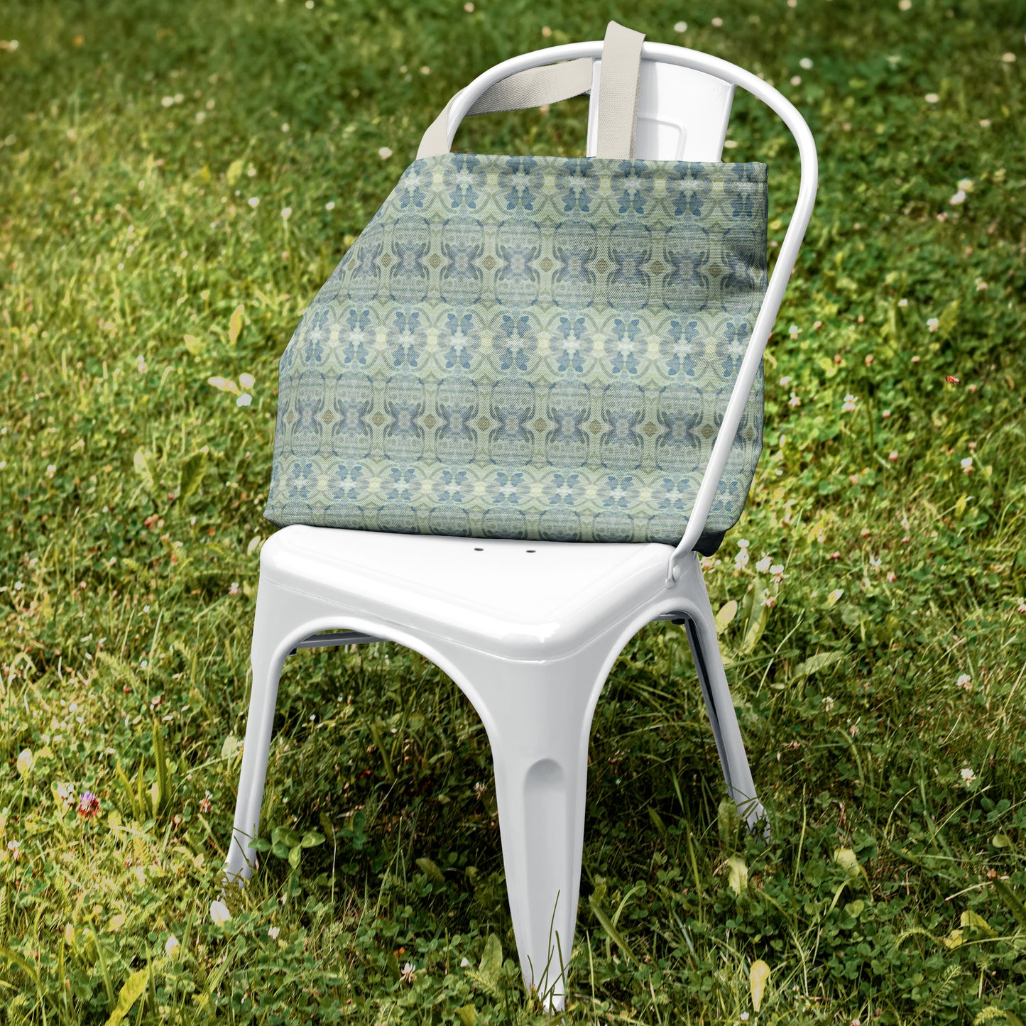 Canvas tote bag featuring an abstract blue and green pattern sitting on a white metal chair in green grass