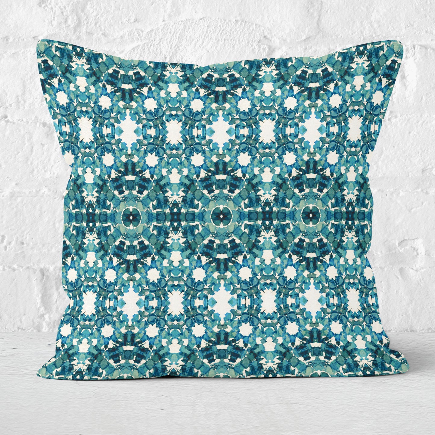 Square throw pillow featuring an abstract teal pattern, sitting against a white brick wall