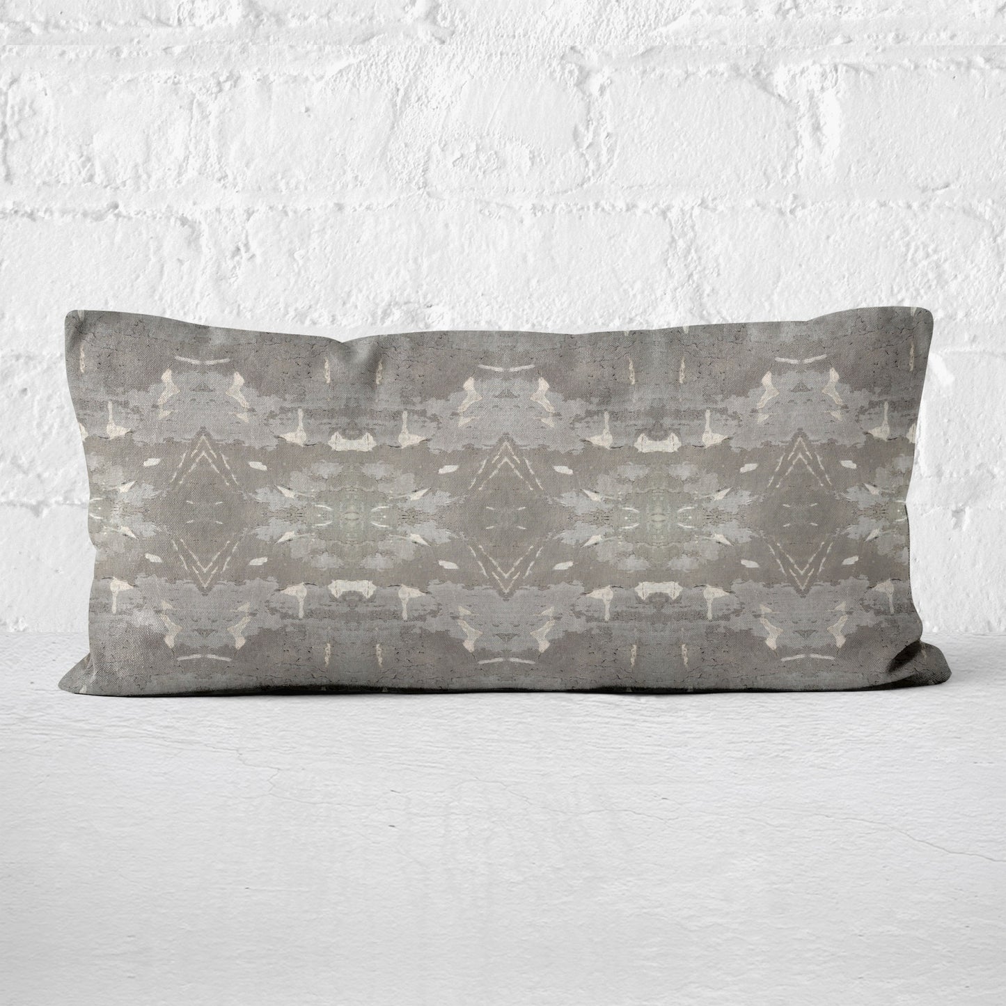 Lumbar pillow featuring a grey abstract geometric pattern leaning against a white brick wall