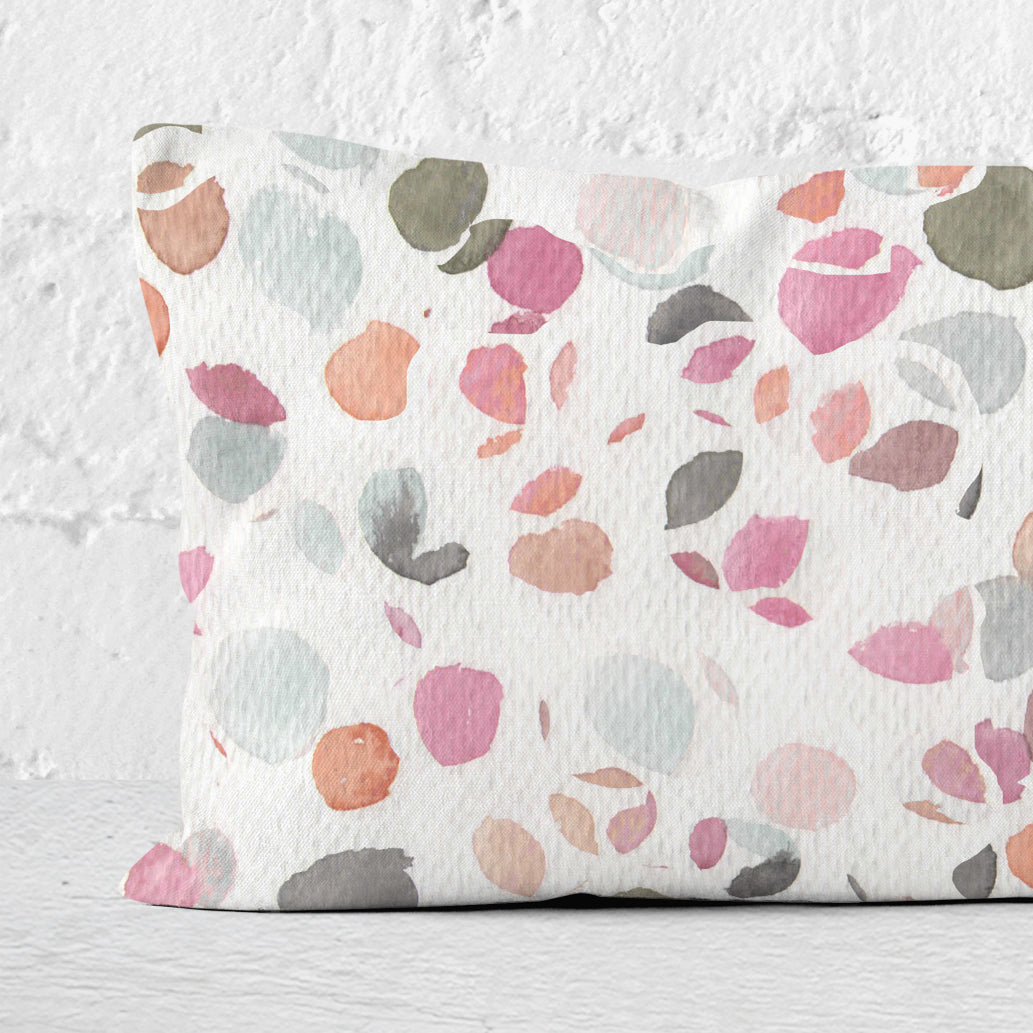 Close up detail of a 12x24 lumbar pillow, featuring an abstract watercolor painting of flower petals, leaning against a white brick wall.