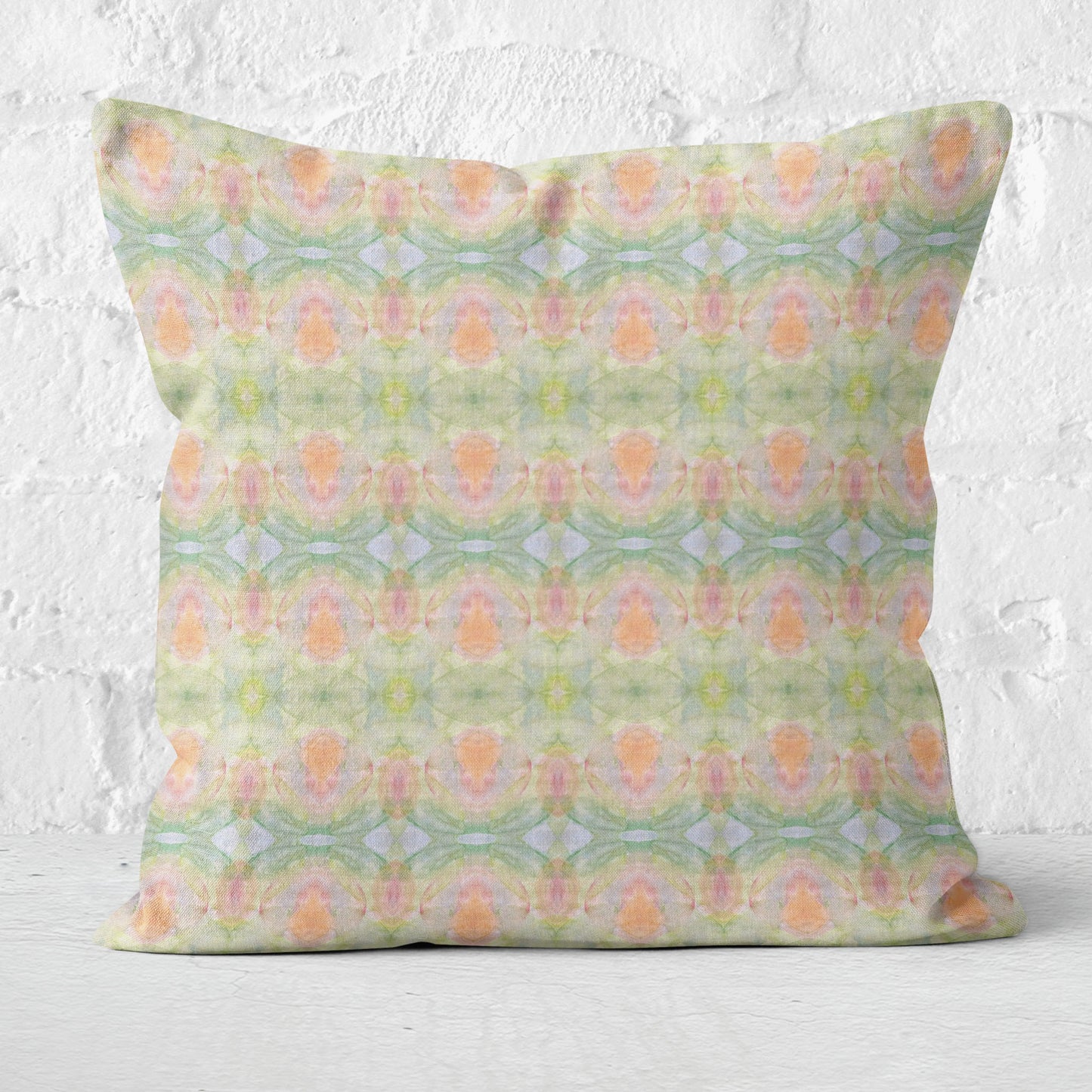 Square throw pillow featuring a hand-painted abstract pattern in pastel colors, sitting in front of a white brick wall