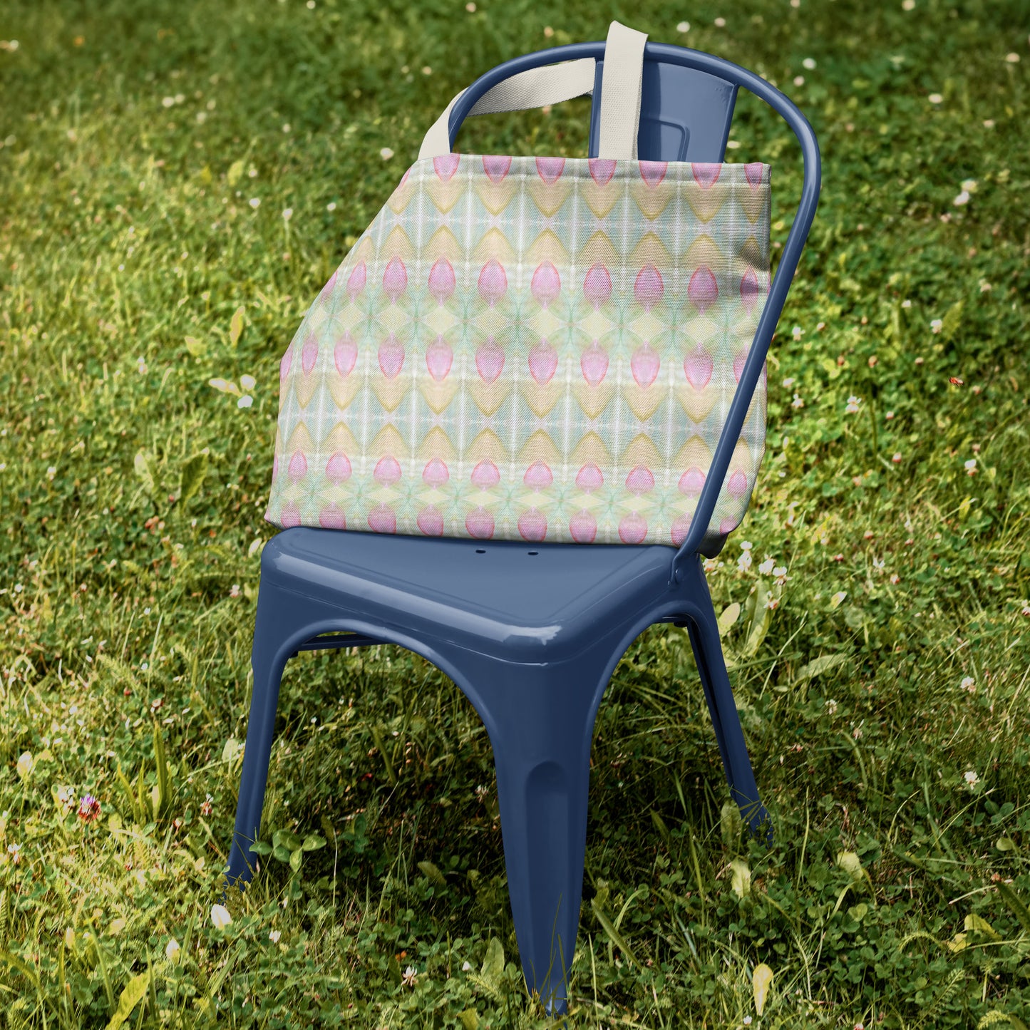 Canvas tote bag featuring a multicolored pastel abstract floral design, sitting on blue chair in green grass