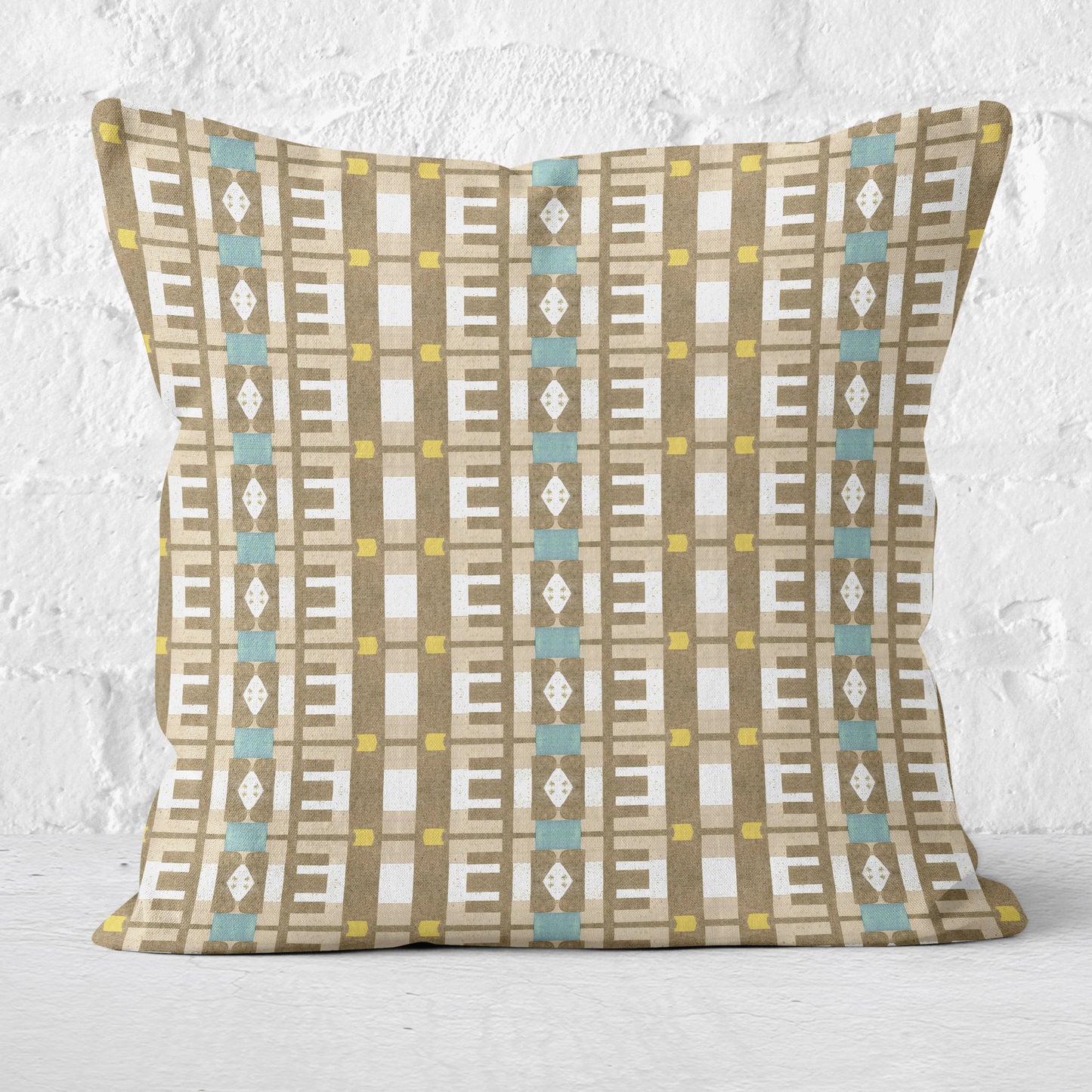 Throw pillow featuring a geometric tan and white pattern against a white brick wall