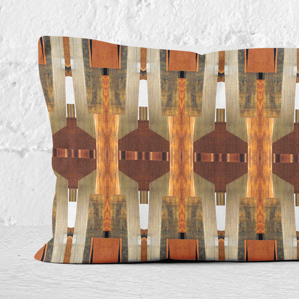 Detail of a 12 x 24 pillow featuring a brown paper collage pattern leaning against a white brick wall.
