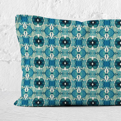 Detail of a 12 x 24 lumbar pillow featuring an abstract hand-painted teal pattern set against a white brick wall.
