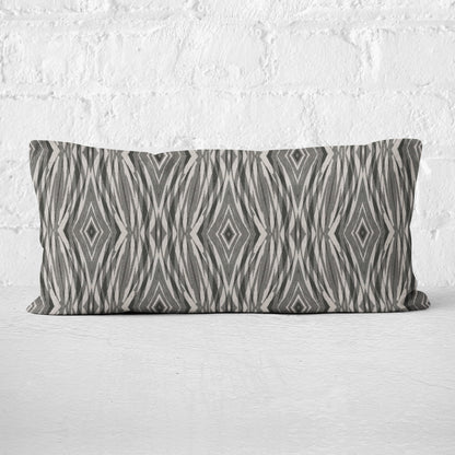 Rectangular lumbar pillow featuring linocut pattern in grey and neutral tones leaning against a white brick wall.