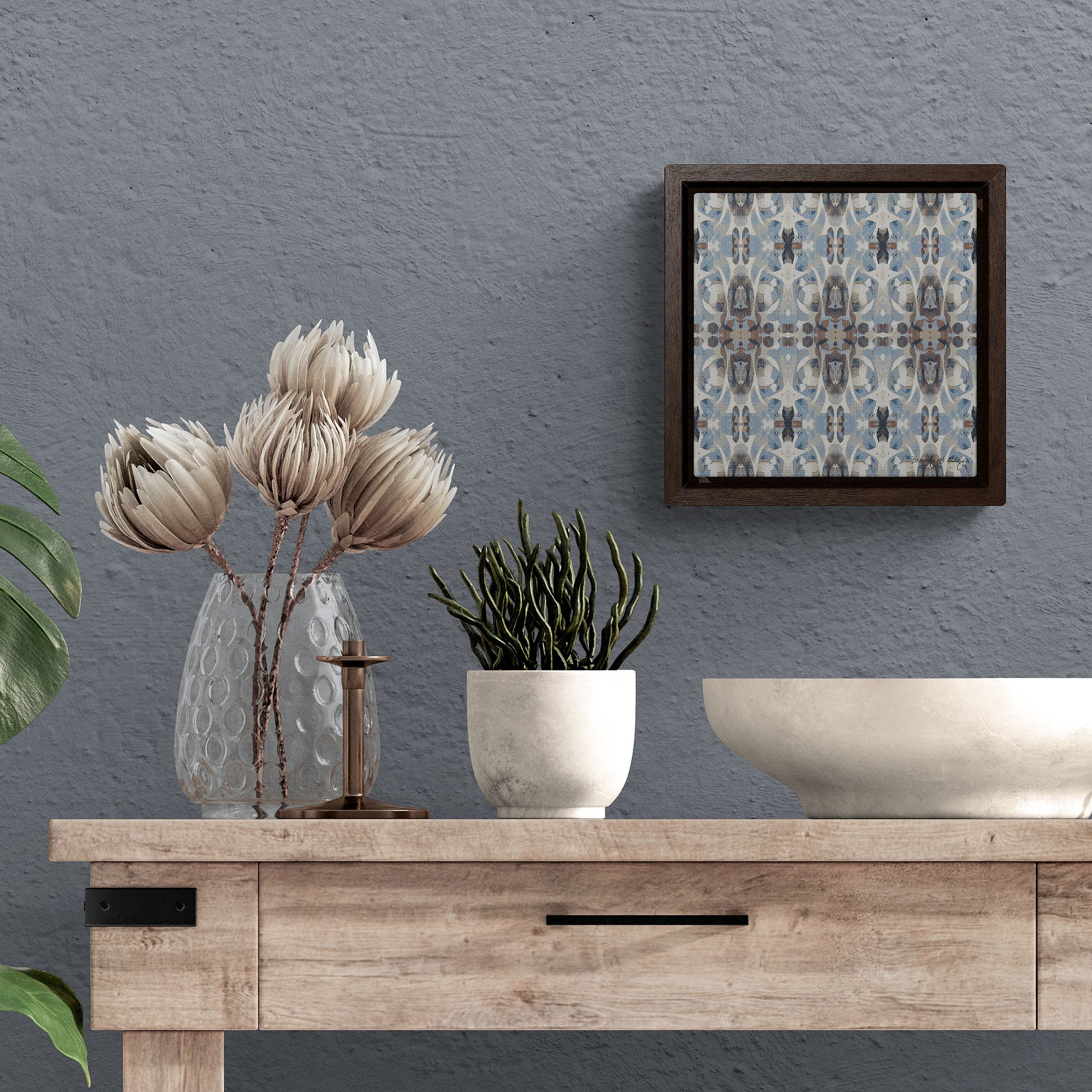 Mini stretch canvas featuring an abstract blue and gray  pattern in a brown fraome hanging against a blue wall