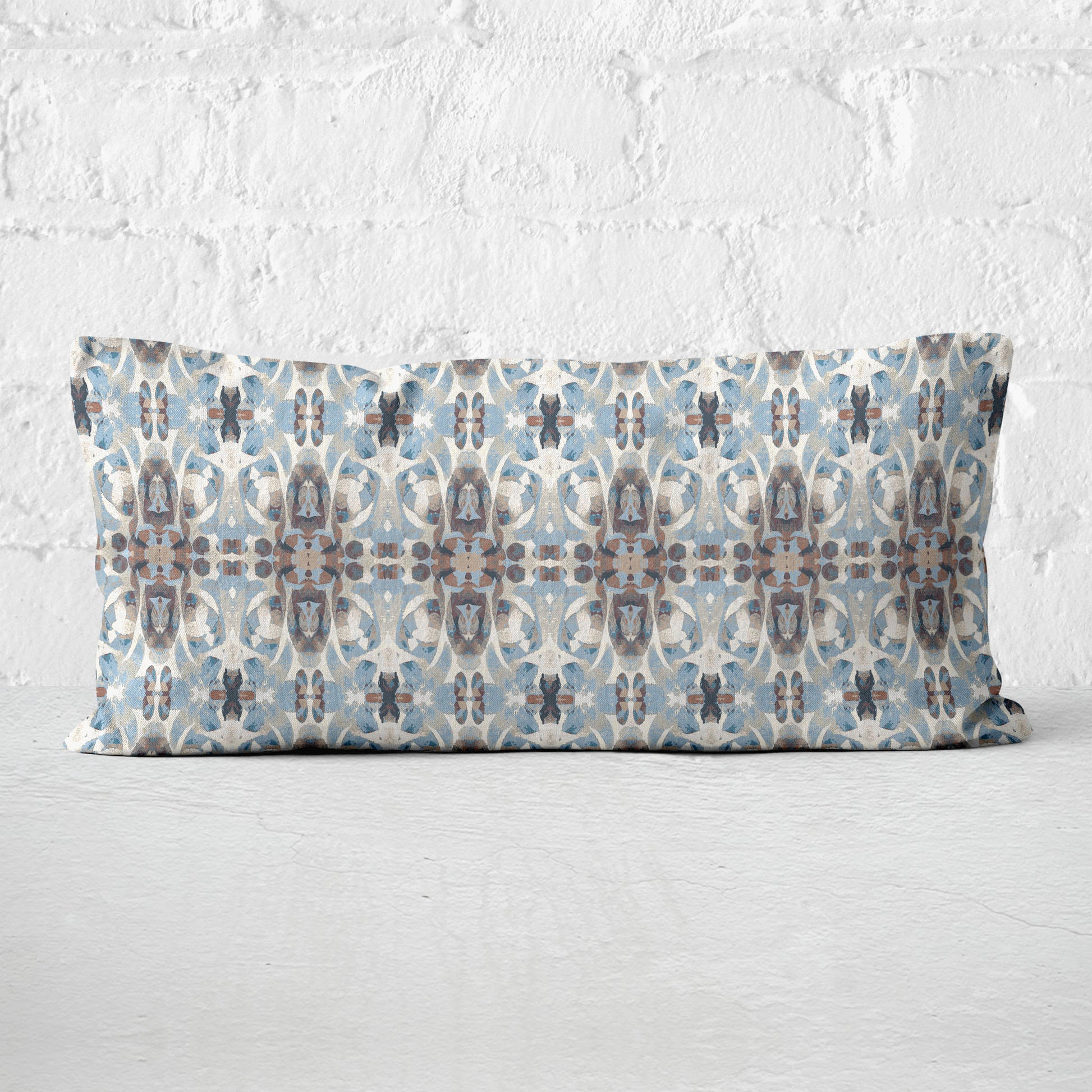 12 x 24 lumbar pillow featuring an abstract hand-painted blue and brown pattern leaning against a white brick wall.