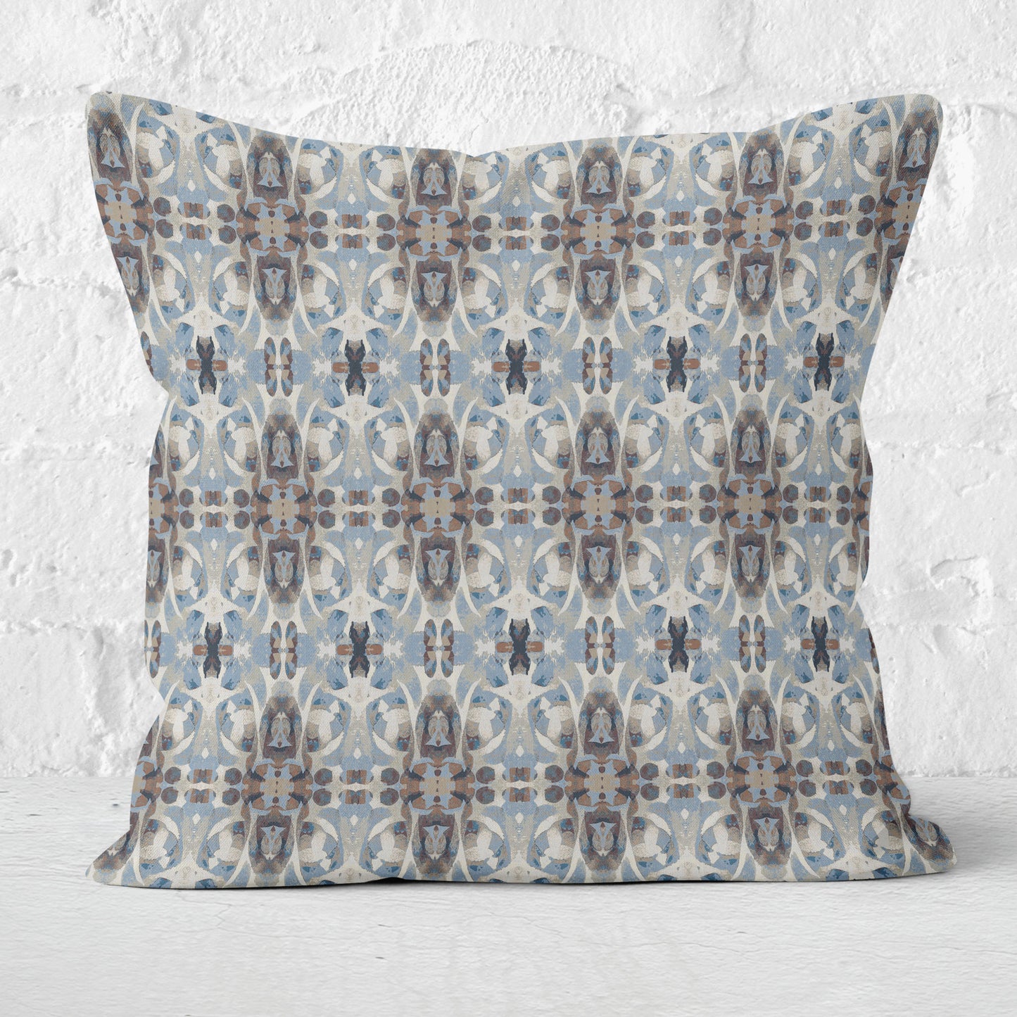 Square throw pillow featuring a blue and brown abstract painted pattern, set against a white brick background