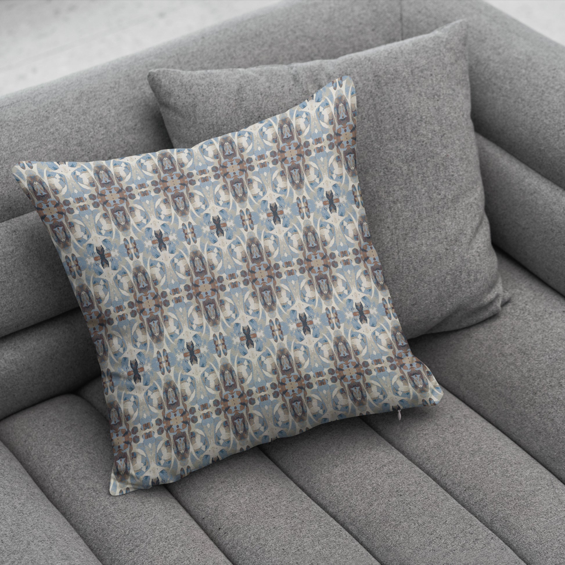 Blue and brown patterned pillow sitting on a gray couch.