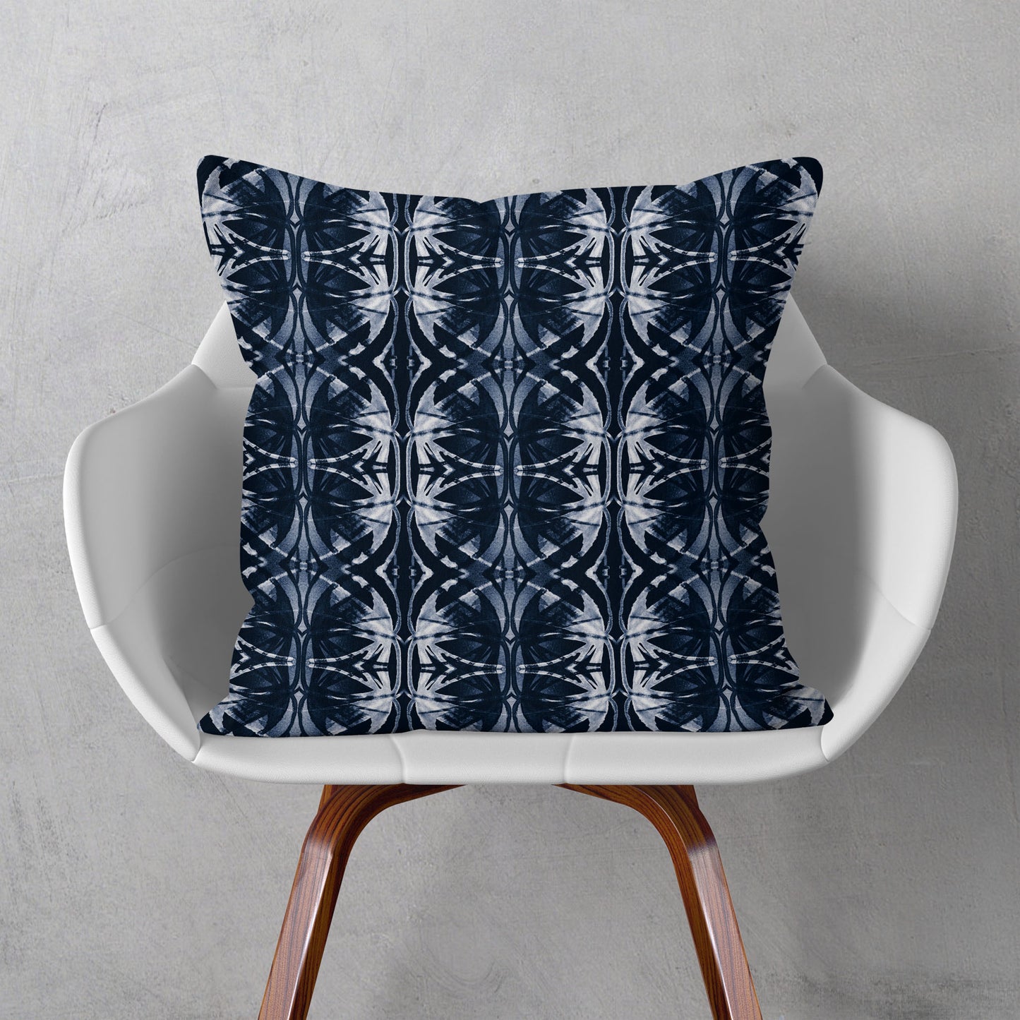 Square throw pillow featuring a dark blue and white abstract pattern, sitting on a  modern white chair