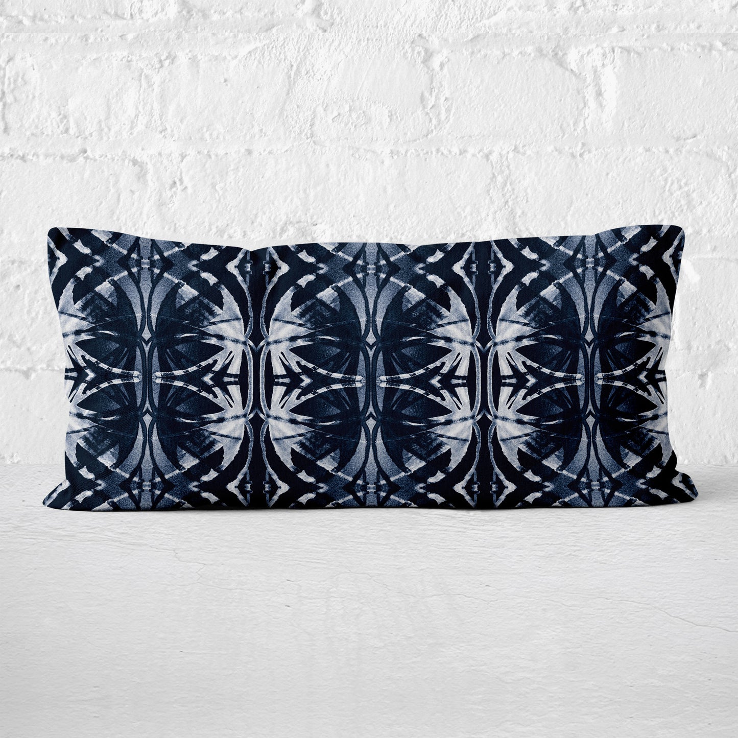 Rectangular pillow featuring abstract pattern in dark blue and white leaning against a white brick wall.