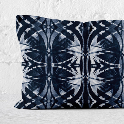Detail of a rectangular pillow featuring abstract pattern in dark blue and white leaning against a white brick wall.