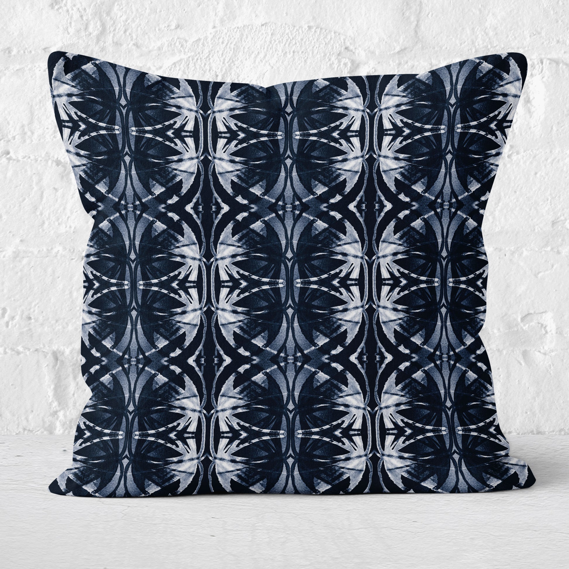 Square throw pillow featuring a dark blue and white abstract pattern sitting against a white brick background