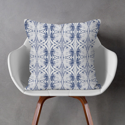 Blue and white abstract pattern pillow sitting on a white chair against a gray wall.