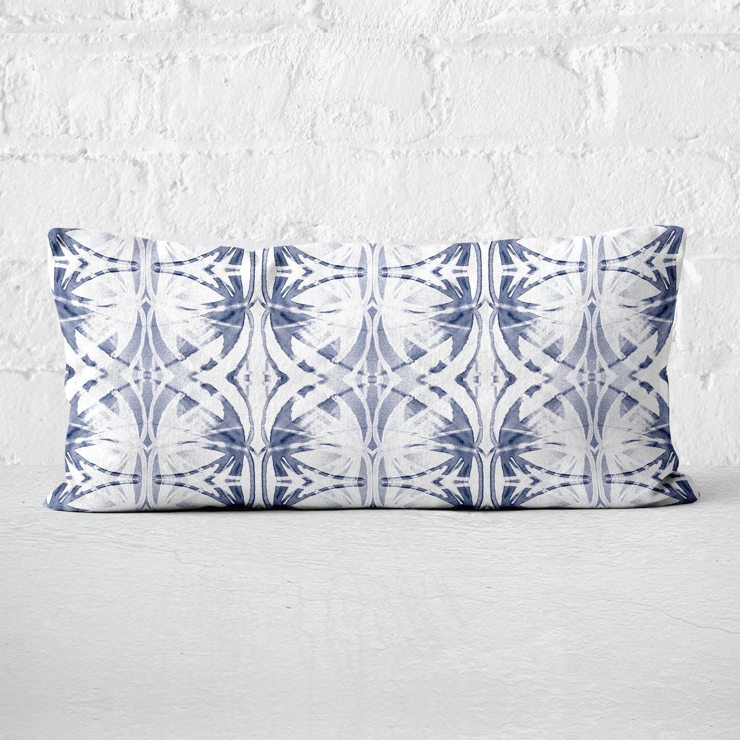 Rectangular pillow featuring abstract painted pattern in light blue and white set against a white brick wall.