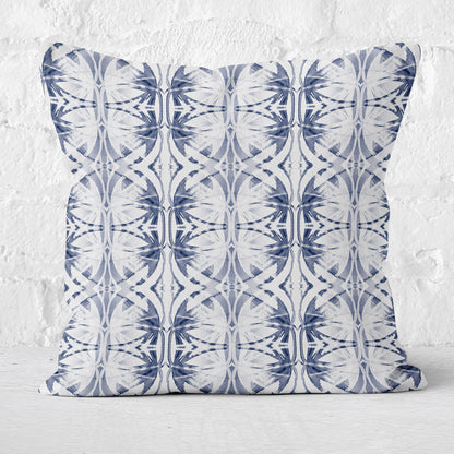 Throw pillow featuring abstract hand painted pattern in blue and white with brick wall in background