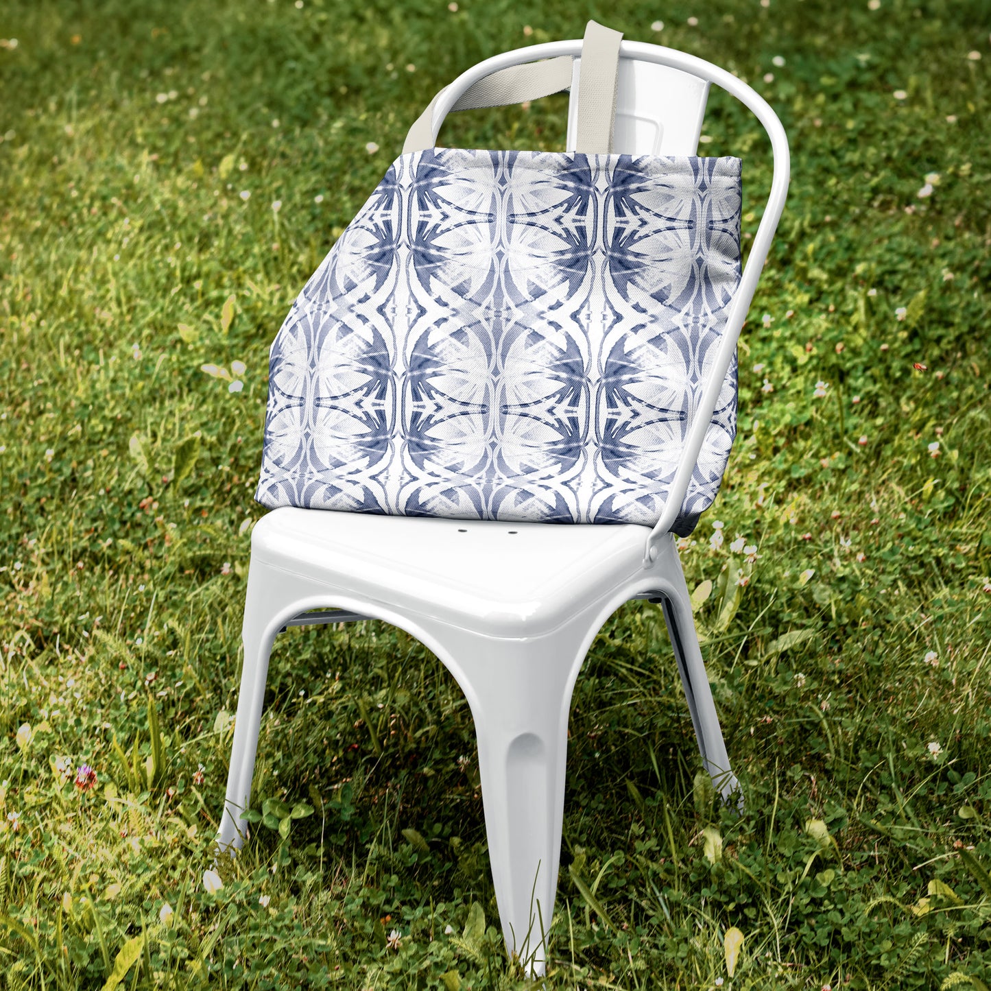 Blue and white pattern tote bag sitting on a white metal chair in green grass