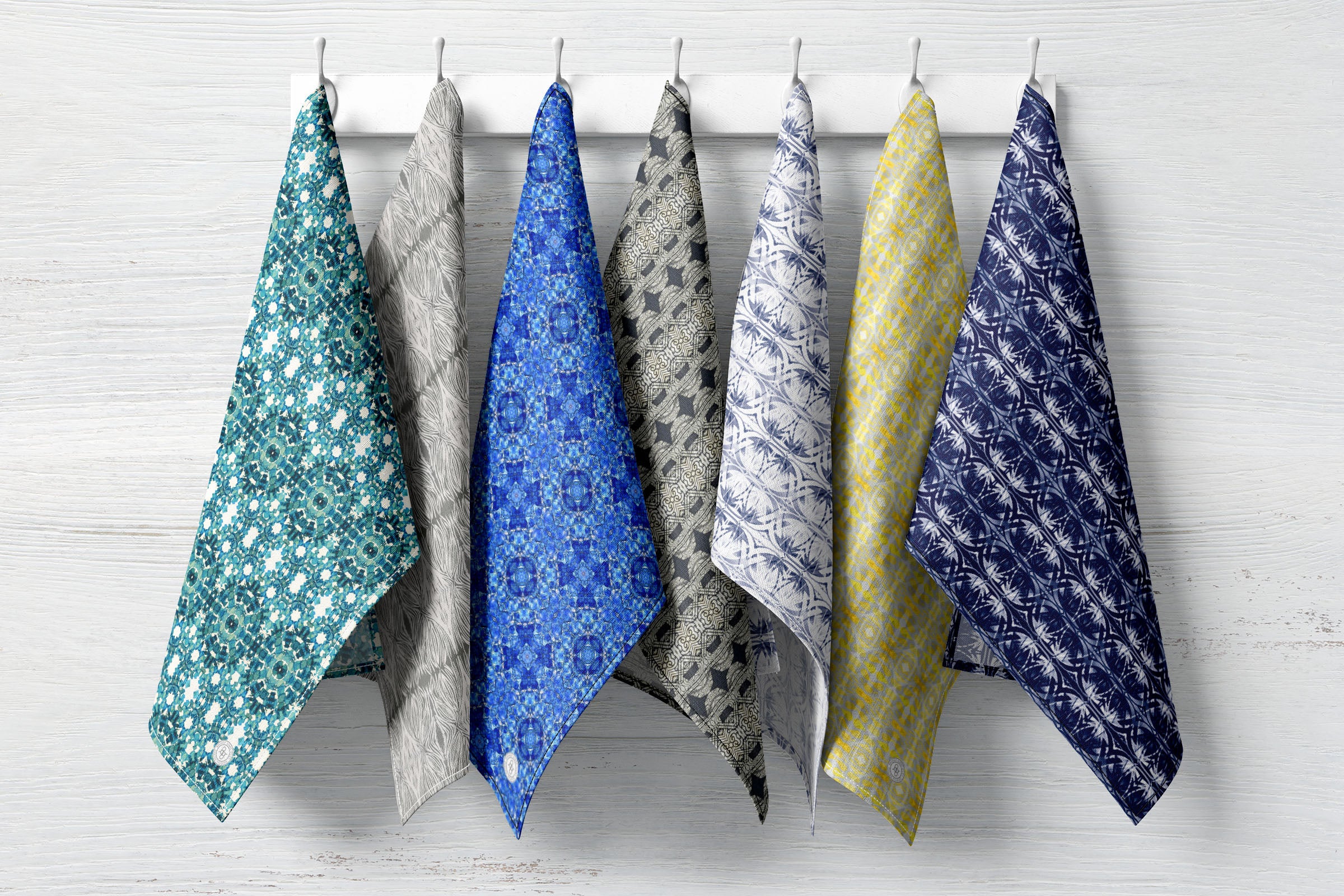 Collection of tea towels hanging on hooks, featuring hand-painted patterns