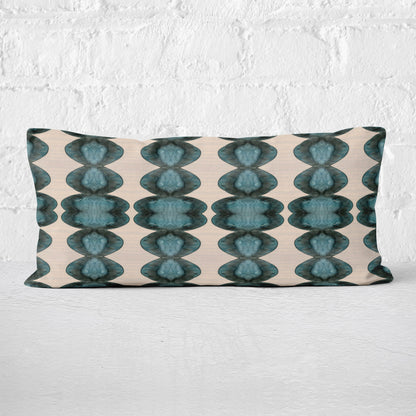Rectangular lumbar pillow featuring abstract hand-painted pattern in blue, black, and cream leaning against a white brick wall.