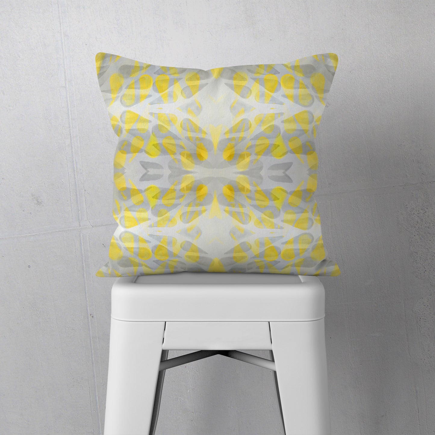 Throw pillow featuring abstract hand-painted pattern in yellow and grey sitting on a white stool.