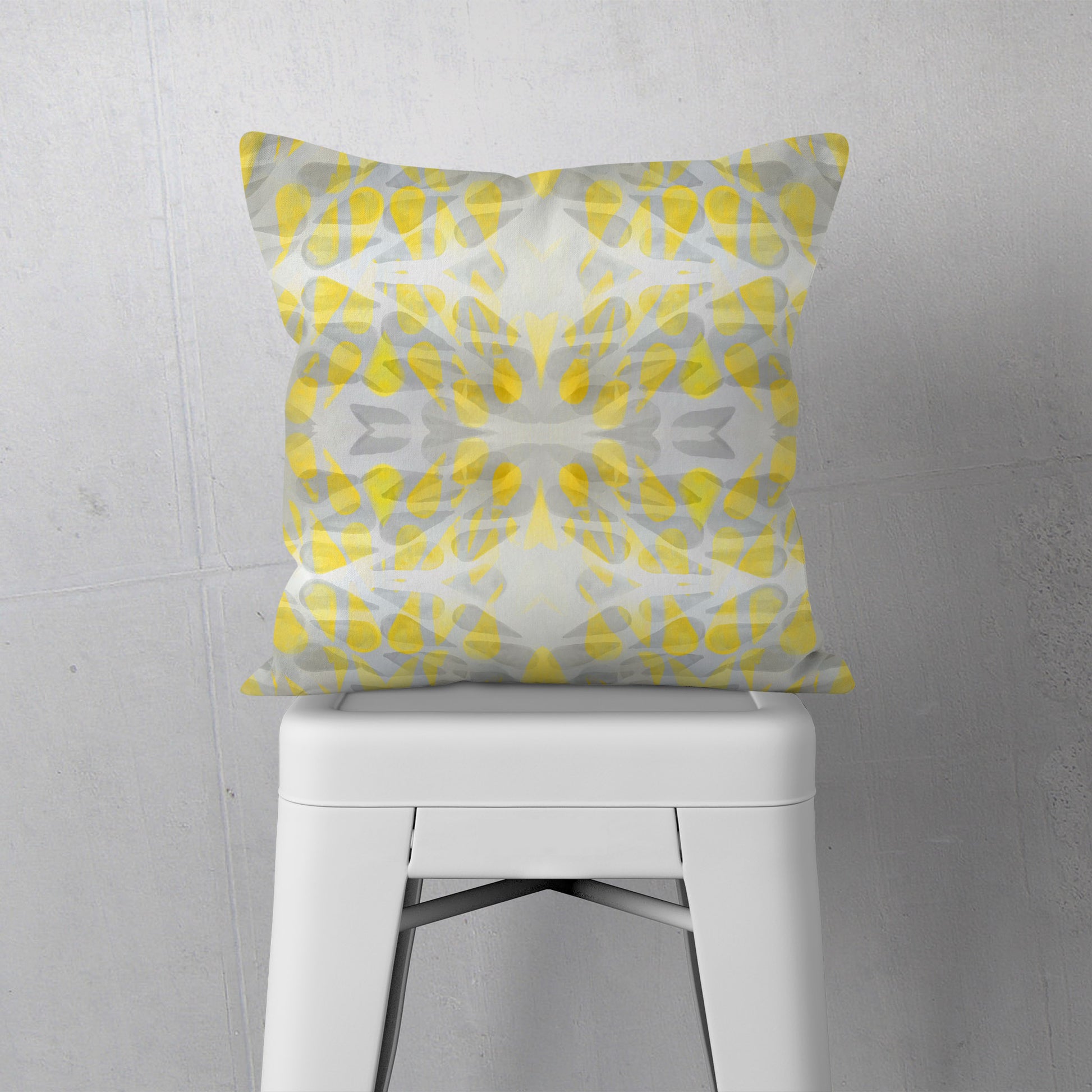 Throw pillow featuring abstract hand-painted pattern in yellow and grey sitting on a white stool.