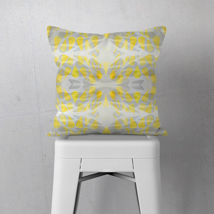 Throw pillow featuring abstract hand-painted pattern in yellow and grey sitting on a white stool.