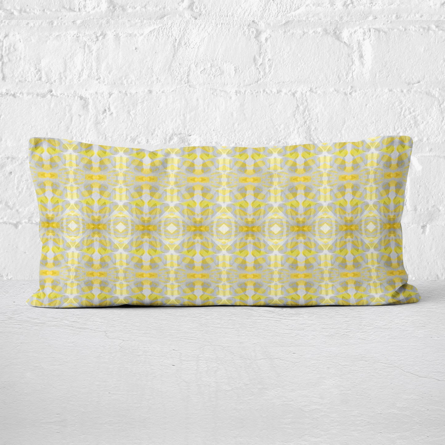 Rectangular lumbar pillow featuring handprinted striped yellow and grey pattern leaning against a white brick wall.