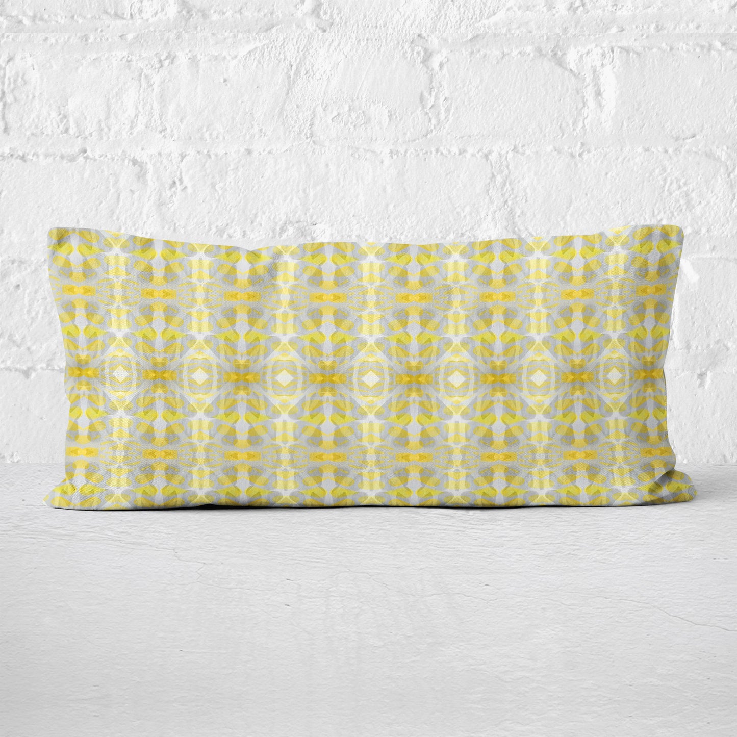 Rectangular lumbar pillow featuring handprinted striped yellow and grey pattern leaning against a white brick wall.