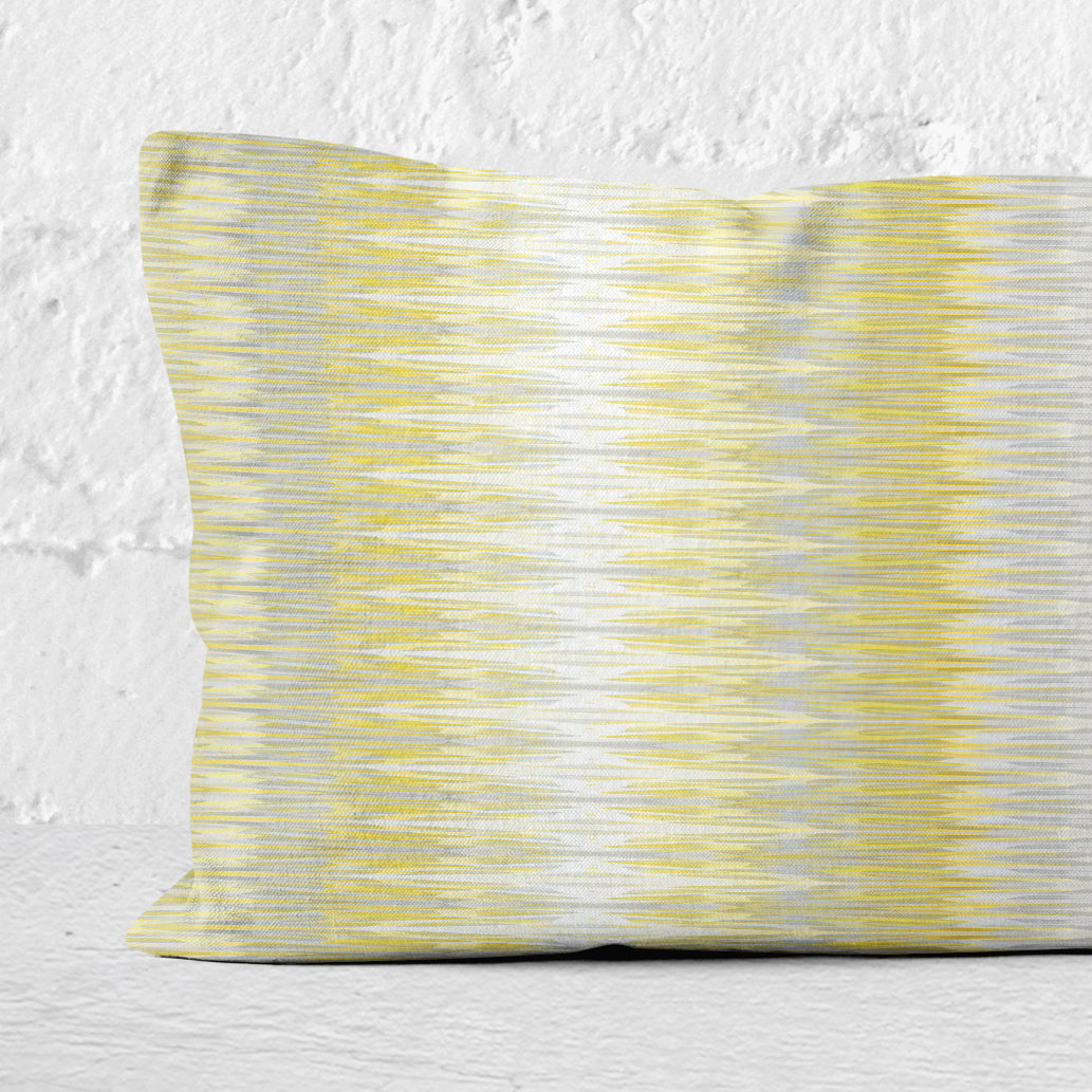 Detail of a rectangular lumbar pillow featuring abstract yellow and gray stripe leaning against a white wall.