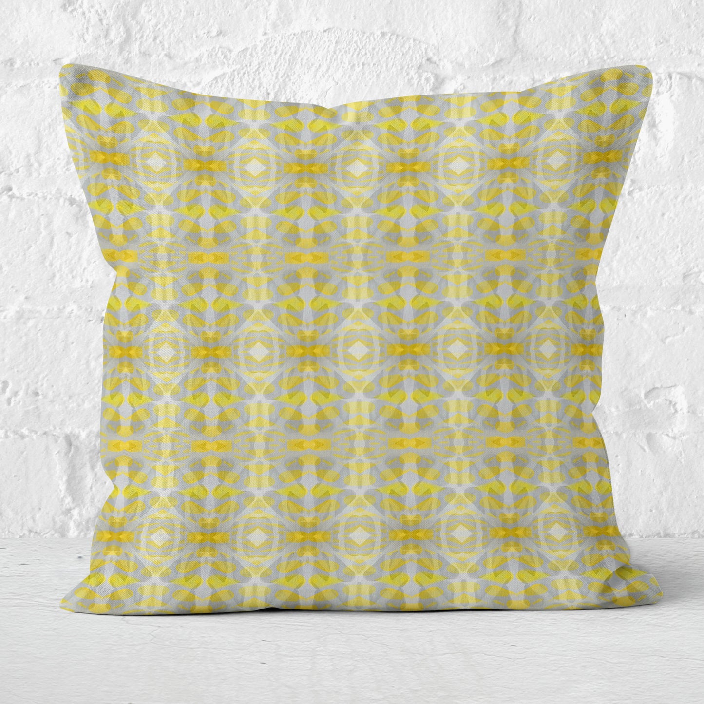 Square throw pillow featuring a yellow and gray abstract pattern leaning against a white brick wall