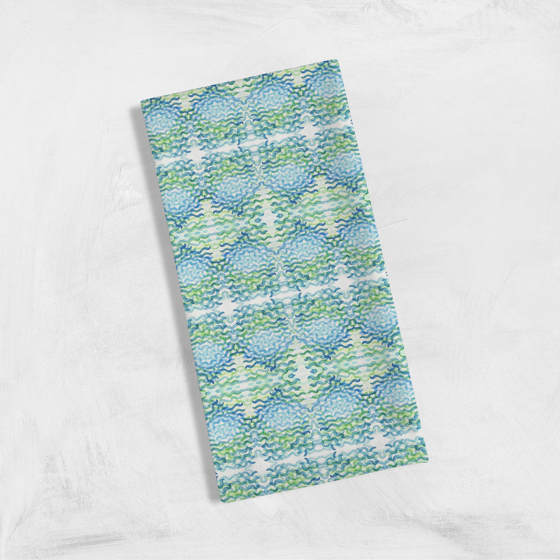 Folded tea towel featuring an abstract blue and green pattern