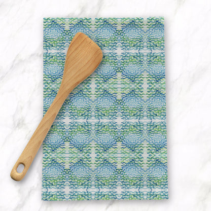 Wooden spoon on top of a folded tea towel featuring a green and blue pattern