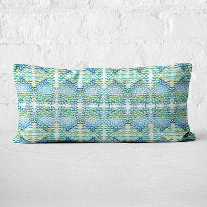 12x24 lumbar pillow featuring an abstract hand-painted pattern in green and blue leaning against a white brick wall.