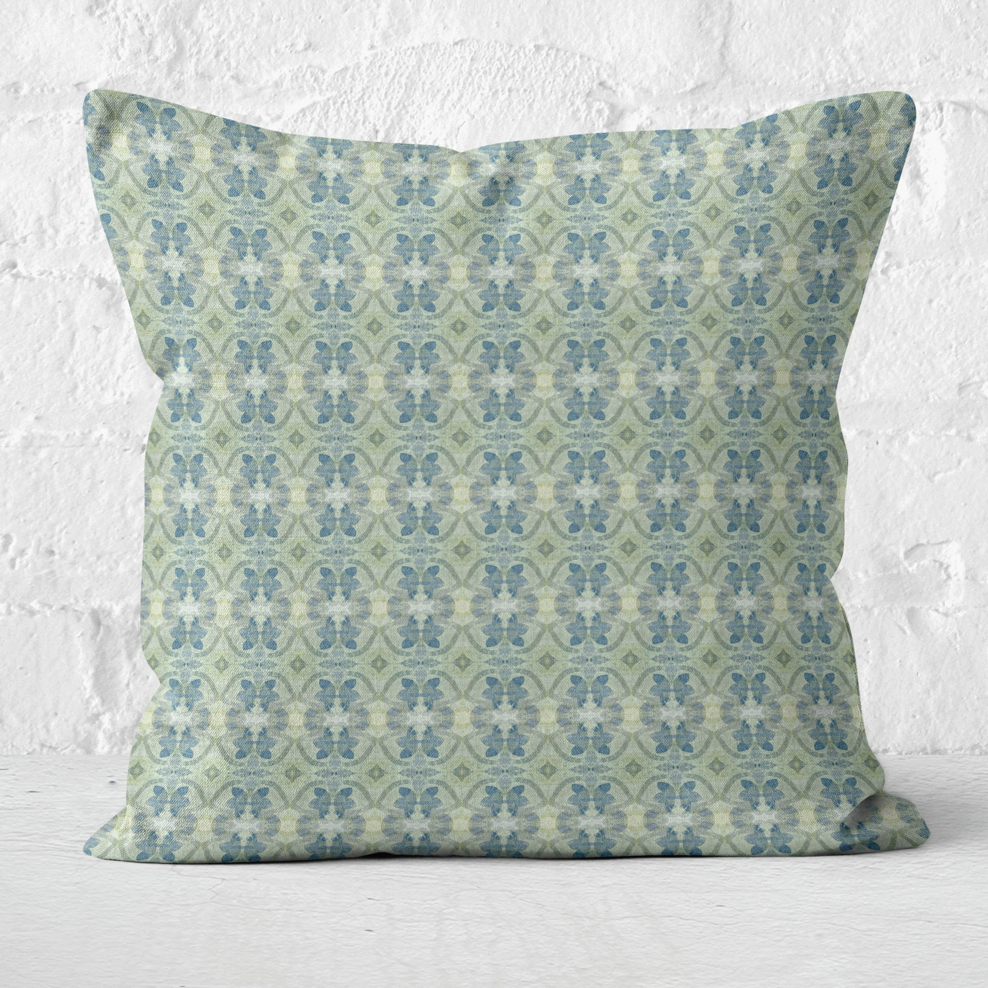 Square throw pillow featuring a blue and green abstract floral pattern set against a white brick wall
