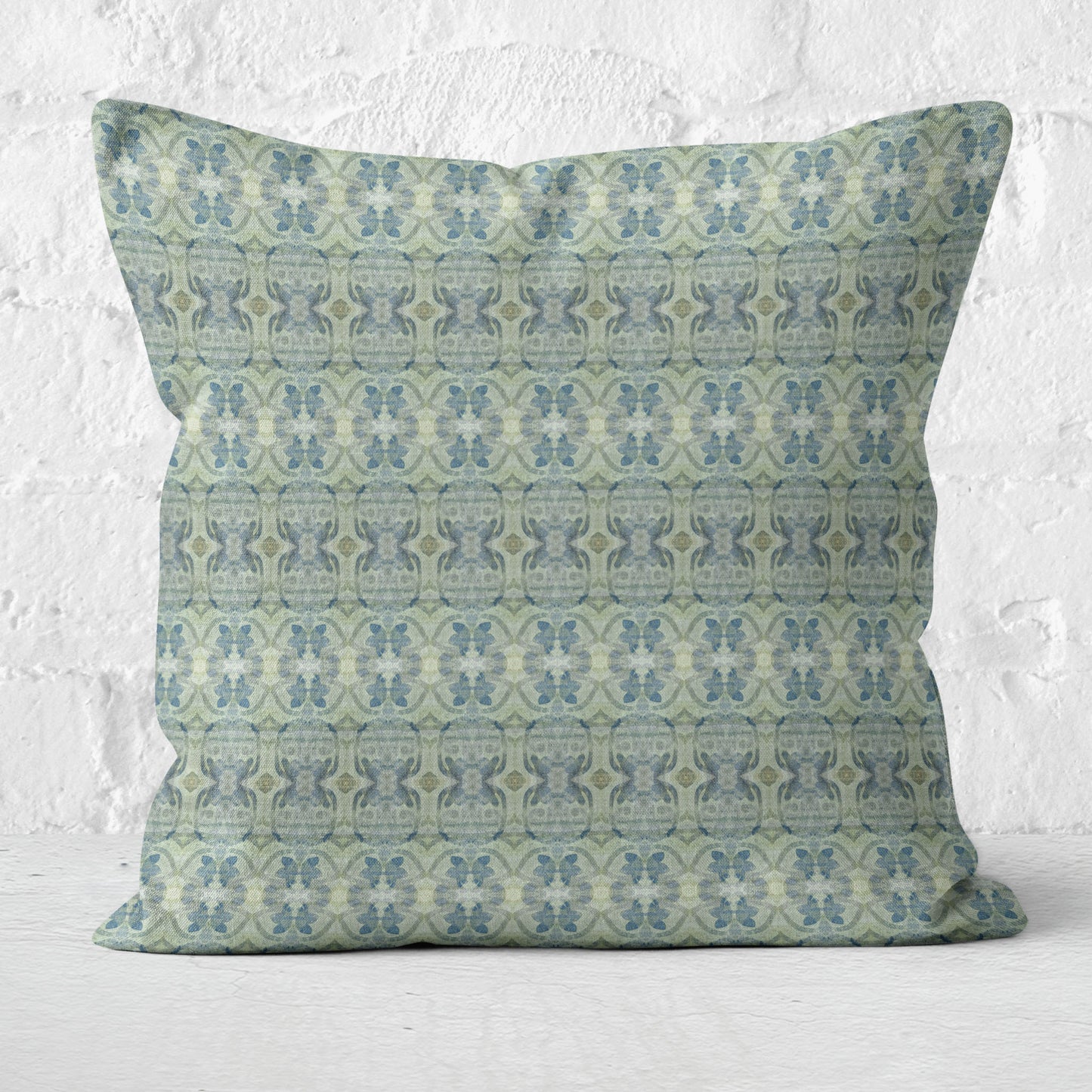 Square throw pillow featuring a blue and green abstract floral pattern sitting against a white brick wall