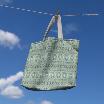 Canvas tote bag featuring an abstract blue and green pattern hanging on a clothesline with blue sky background