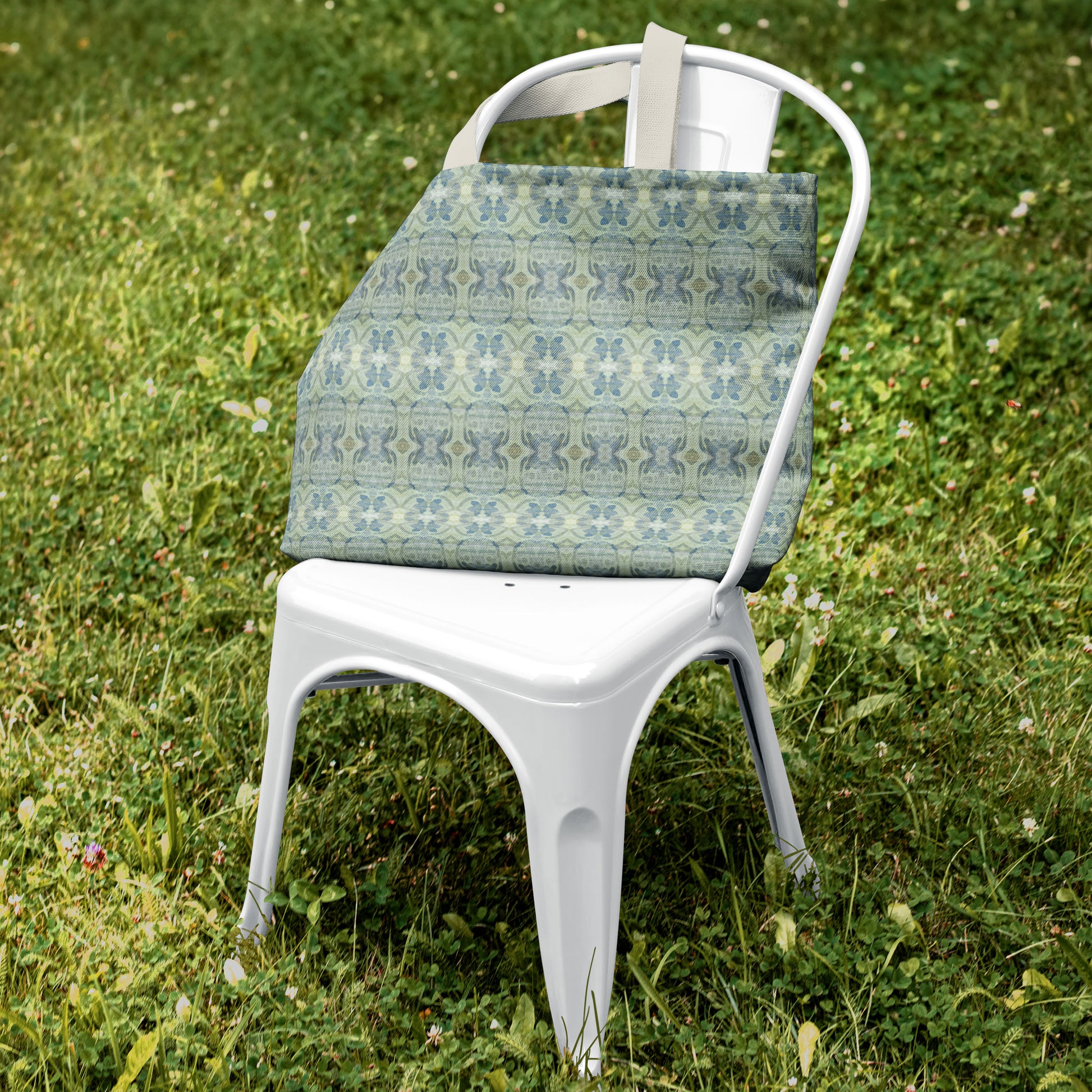 Canvas tote bag featuring an abstract blue and green pattern sitting on a white metal chair in green grass