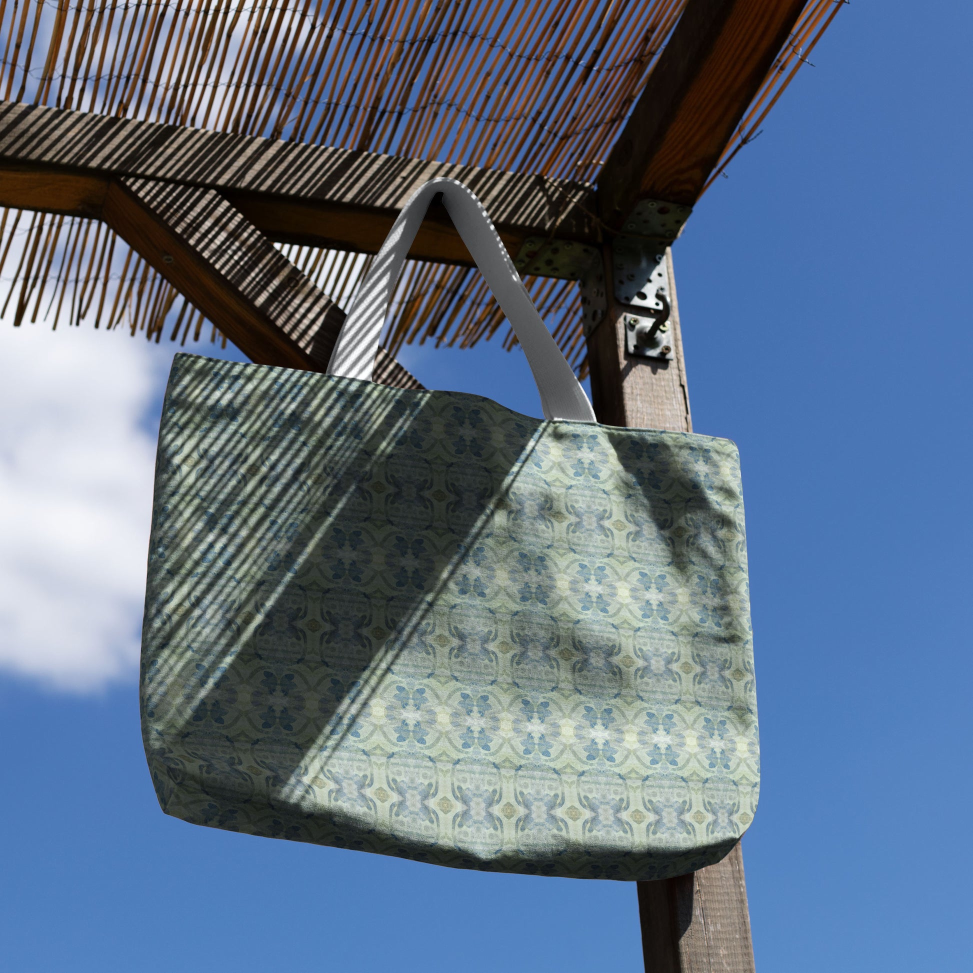 Canvas tote bag featuring an abstract blue and green pattern hanging on a canopy with blue sky background