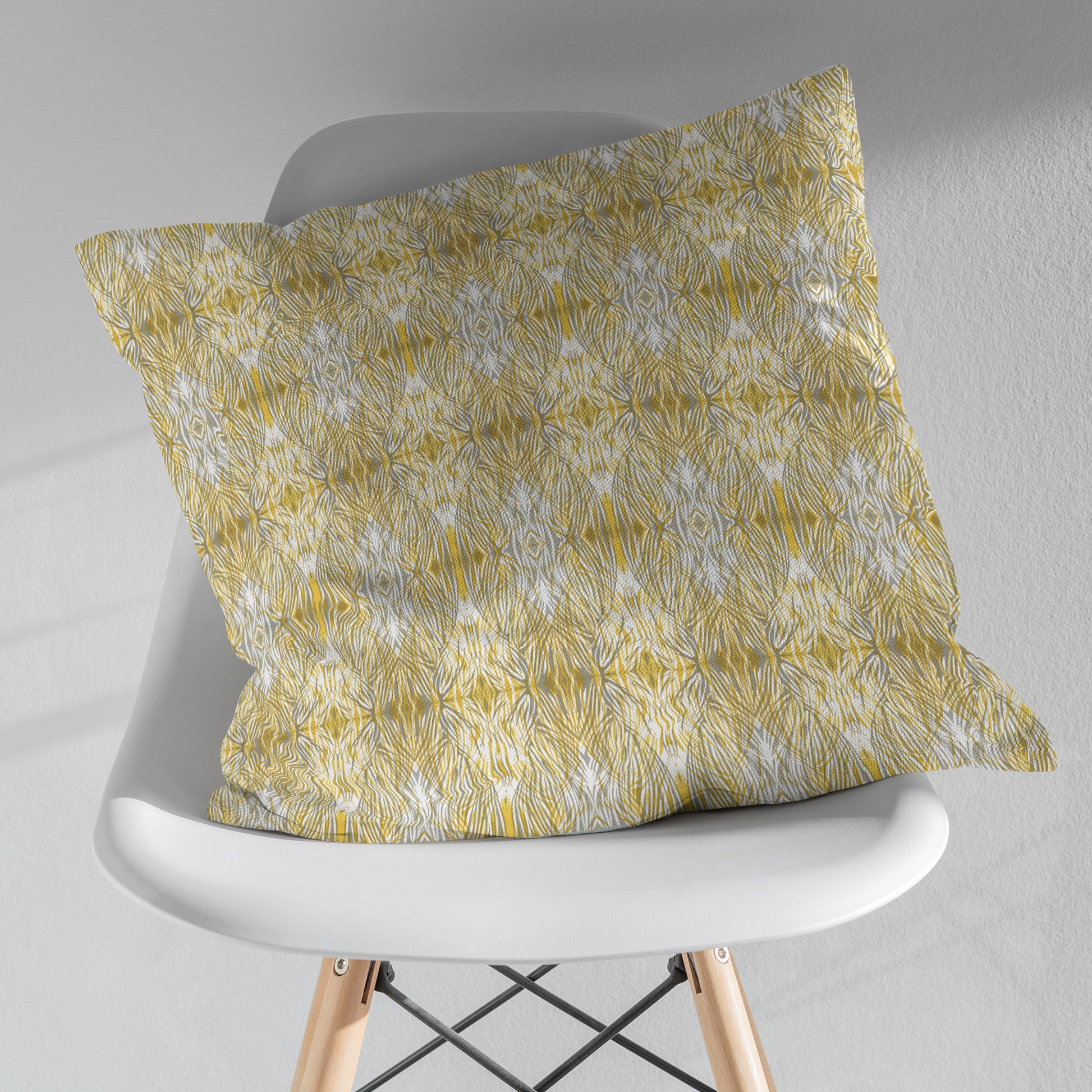 Gold and gray patterned pillow sitting on a white modernist chair