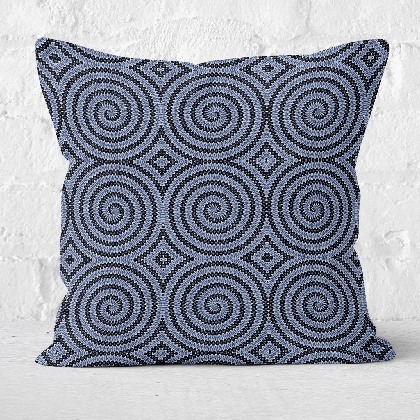 Pillow featuring geometric circular pattern in blue and white with a white brick wall in the background