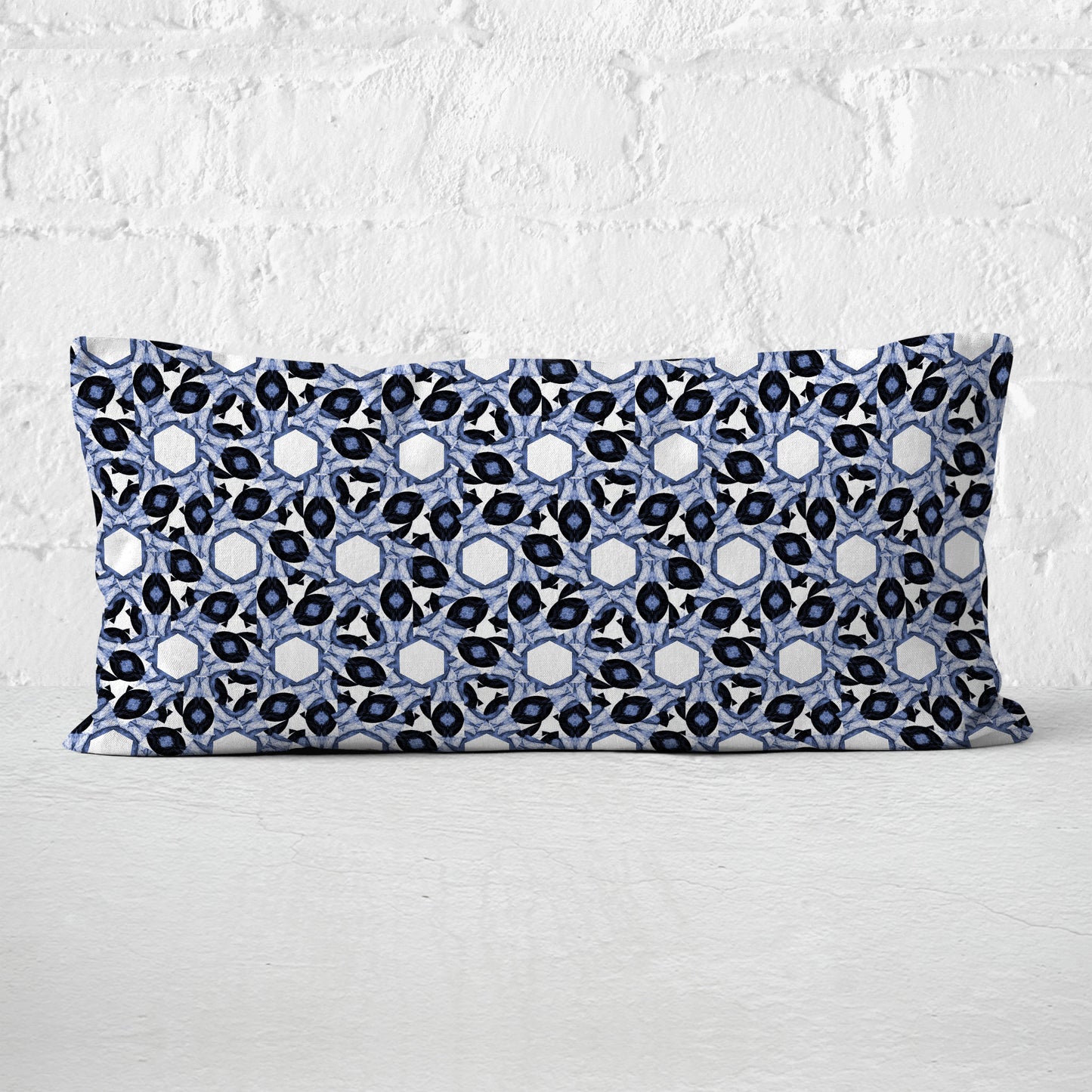 Rectangular lumbar pillow featuring abstract geometric pattern in blue and white leaning against a white brick wall.