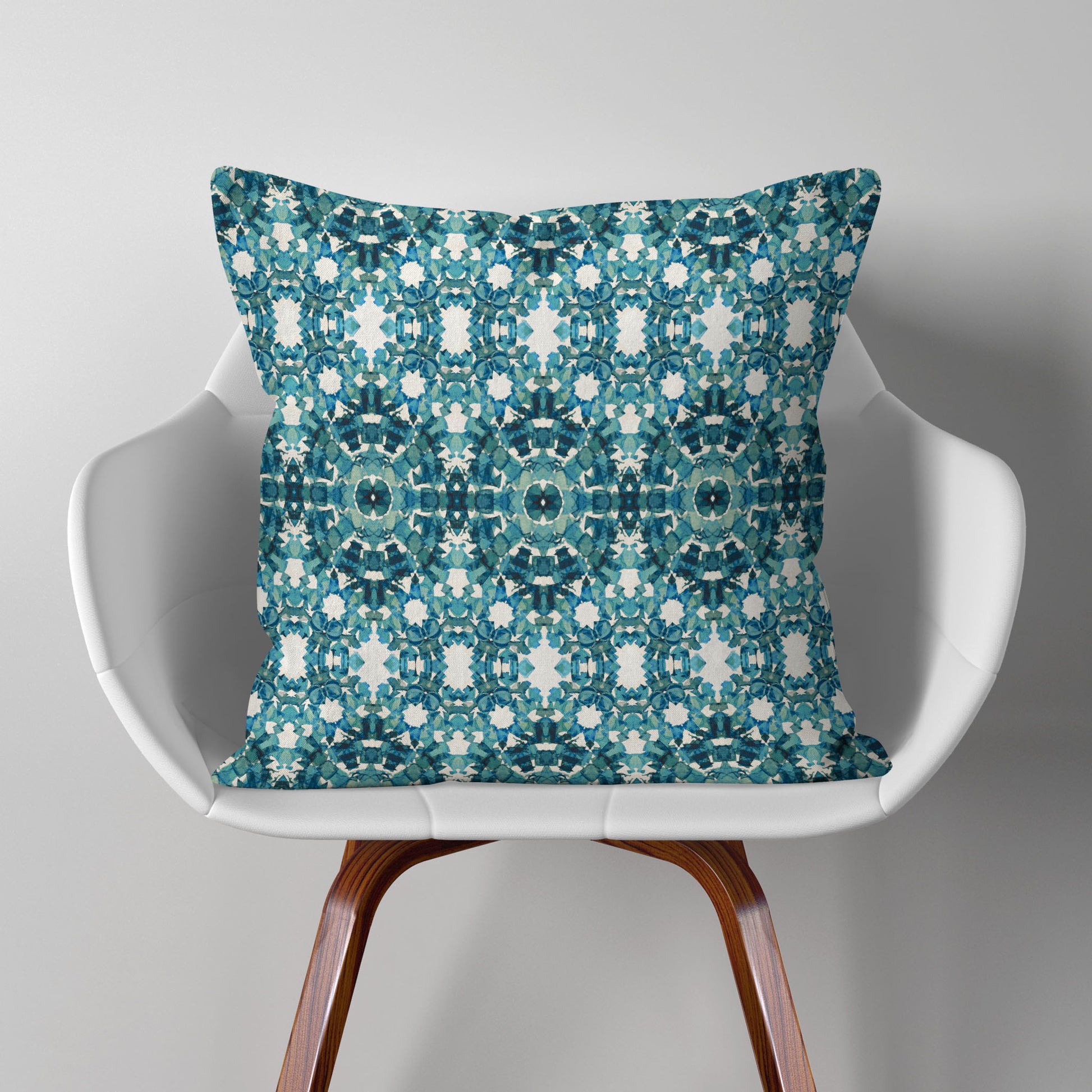 Square throw pillow featuring an abstract teal pattern, sitting on a modern white chair