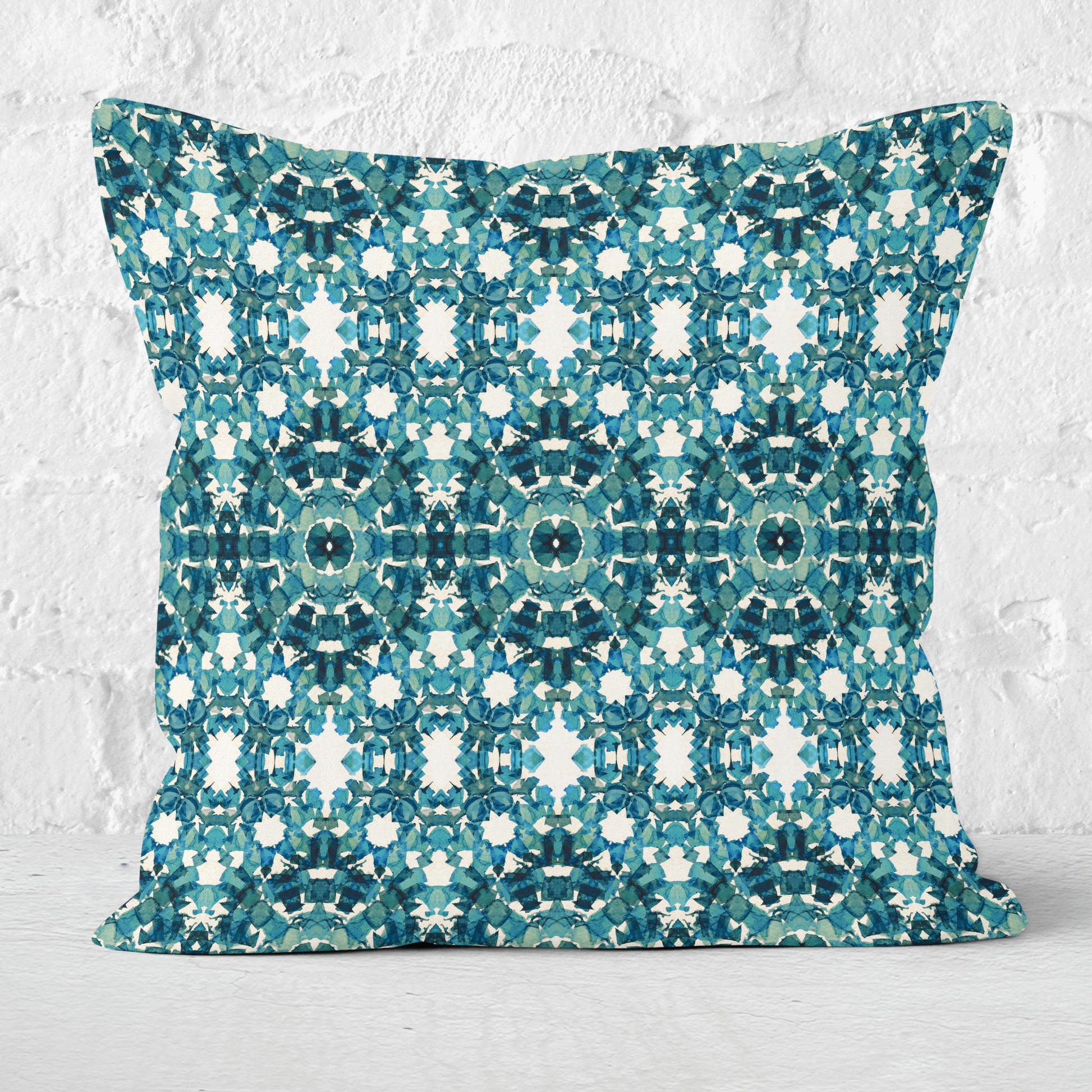 Square throw pillow featuring an abstract teal pattern, sitting against a white brick wall