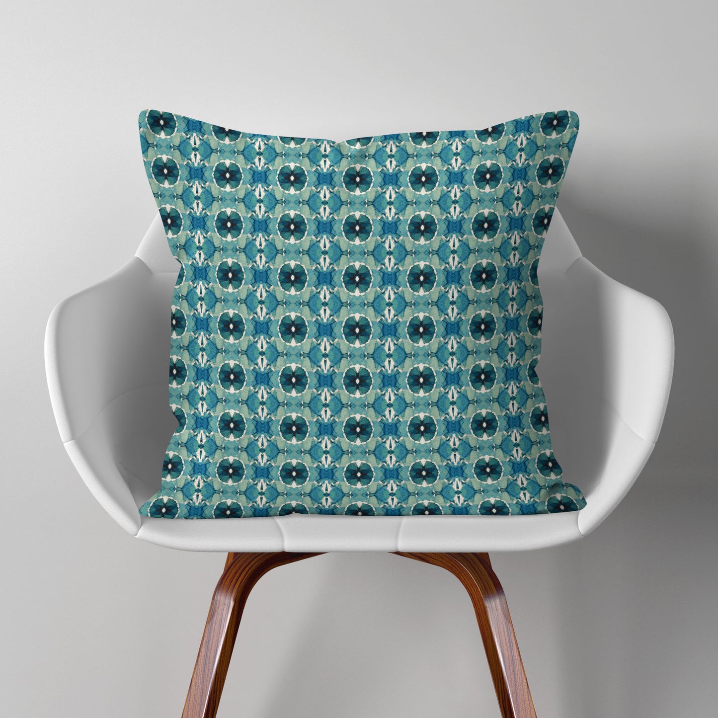 Throw pillow featuring hand-painted geometric pattern in teal, sitting on a modern white chair
