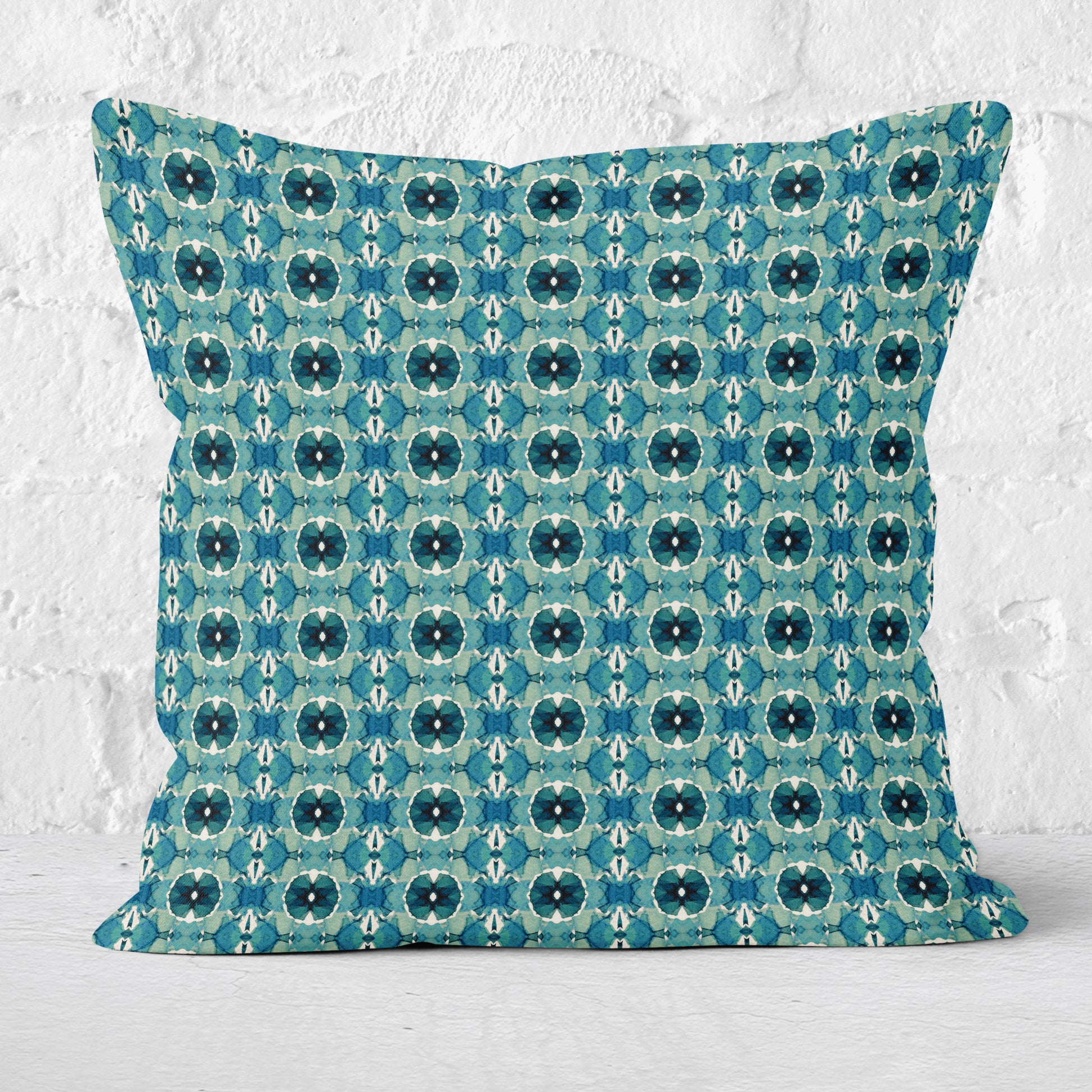 Throw pillow featuring hand-painted geometric pattern in teal with a white brick wall in the background