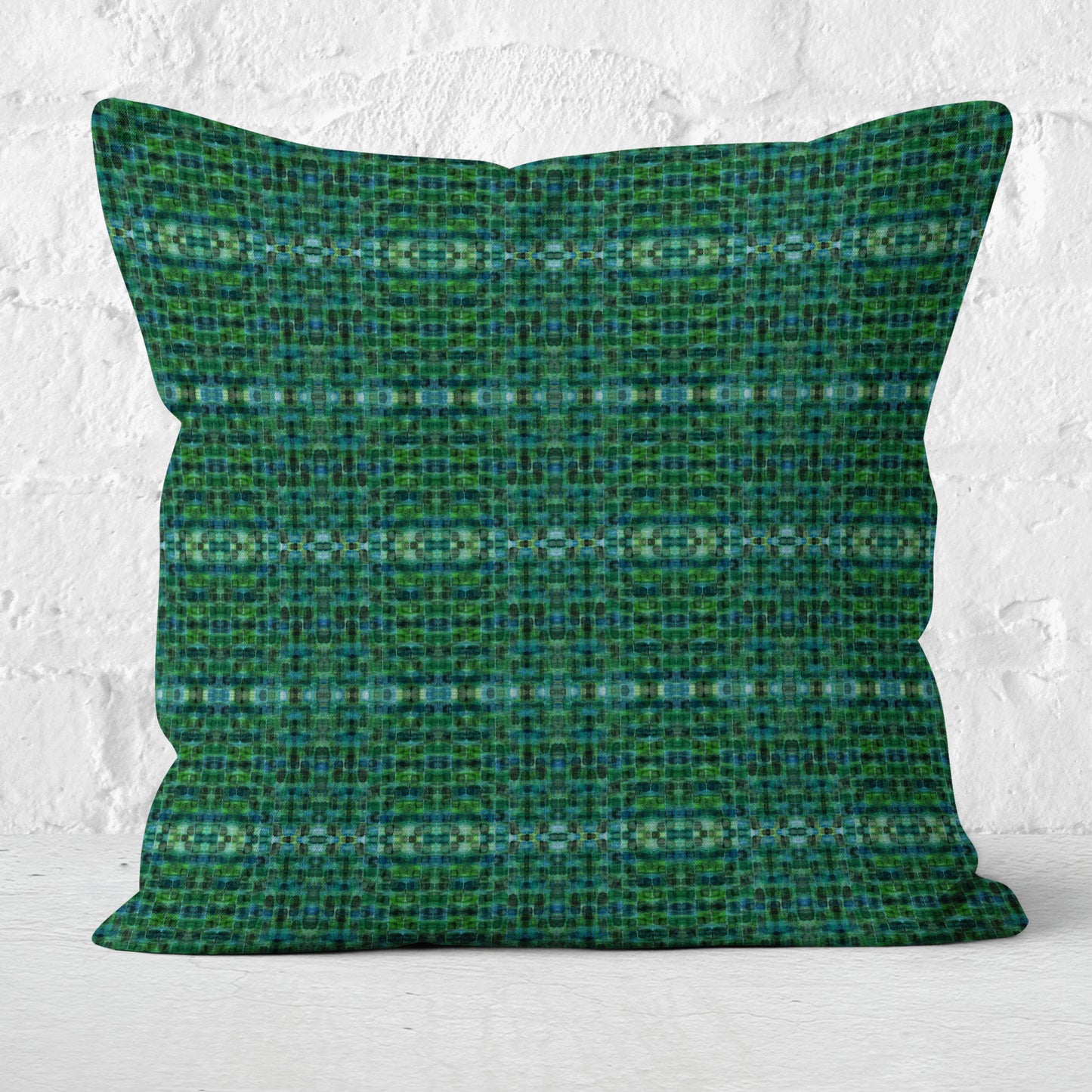 Square pillow featuring a green plaid pattern sitting in front of a white brick wall