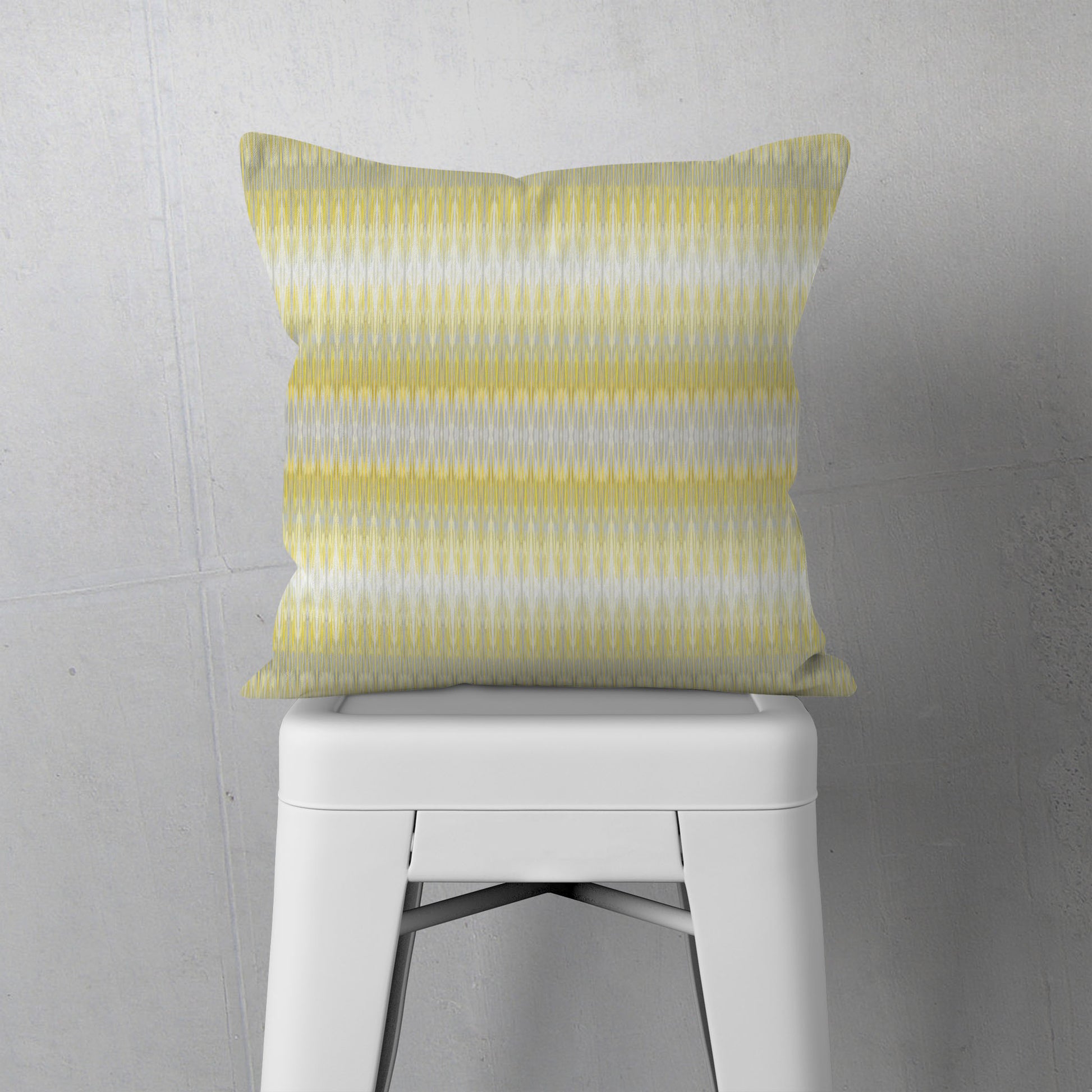 Square pillow featuring hand painted yellow and grey stripe, sitting on a white stool
