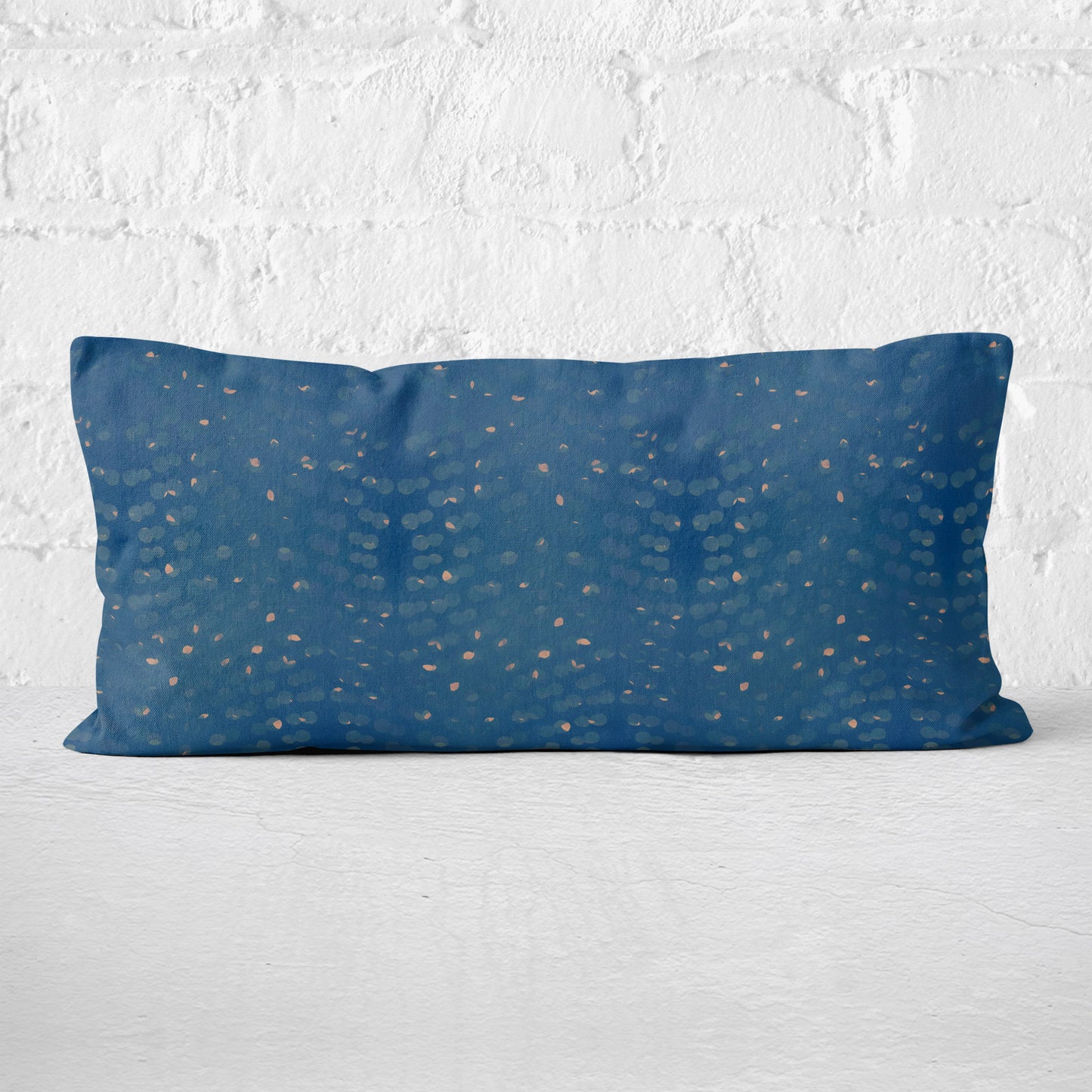 Rectangular lumbar pillow with hand-painted blue and beige pattern against a white brick wall.